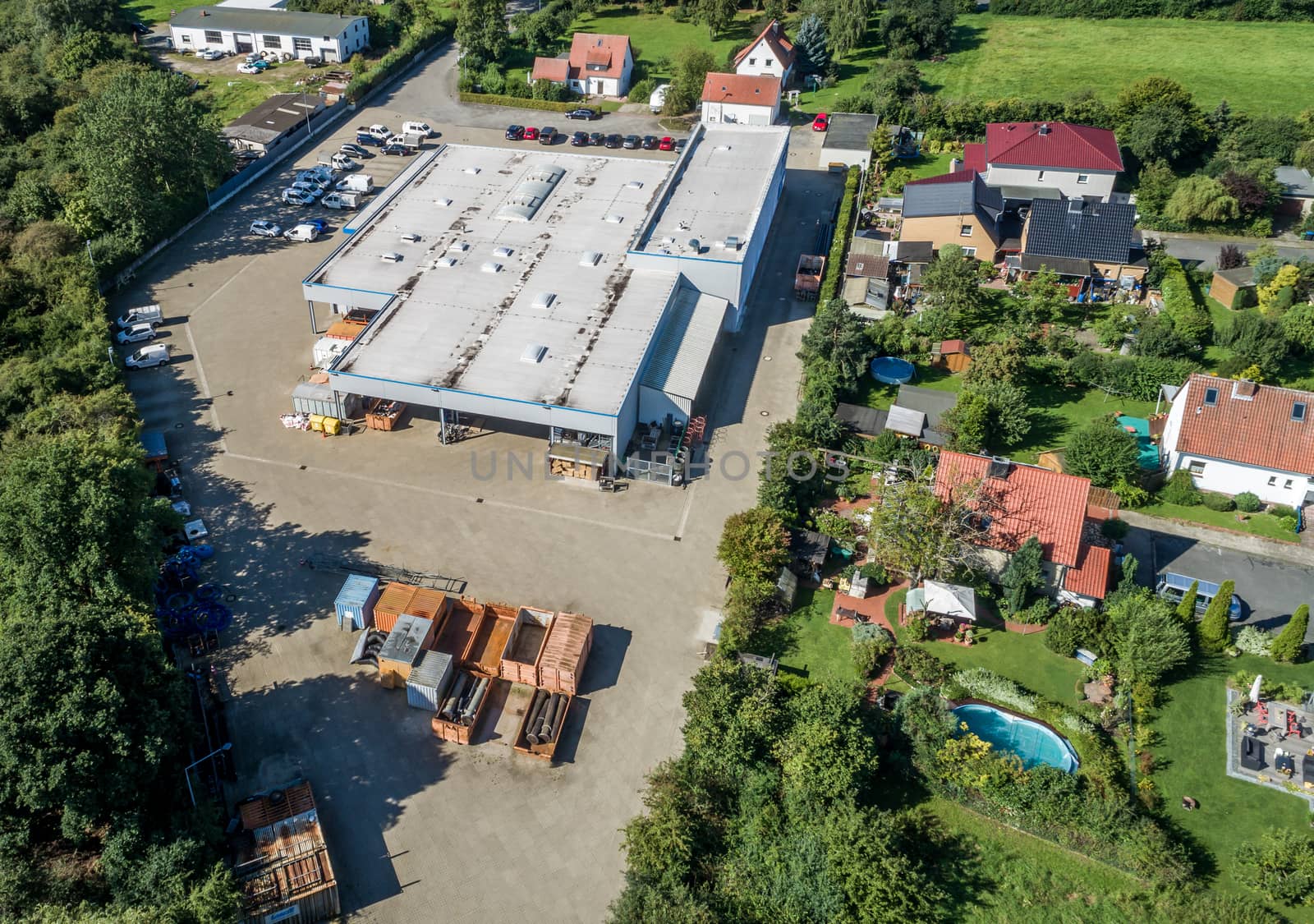 Big industrial hall next to a residential area with detached houses and gardens, aerial view with drone