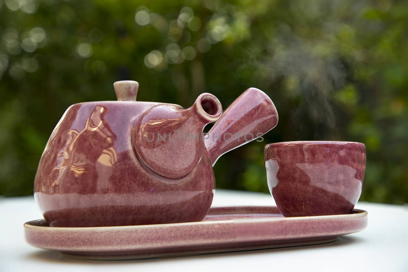 A beautiful, set of chinese style, purple ceramic tea pot and tea cup. Blurry garden background.