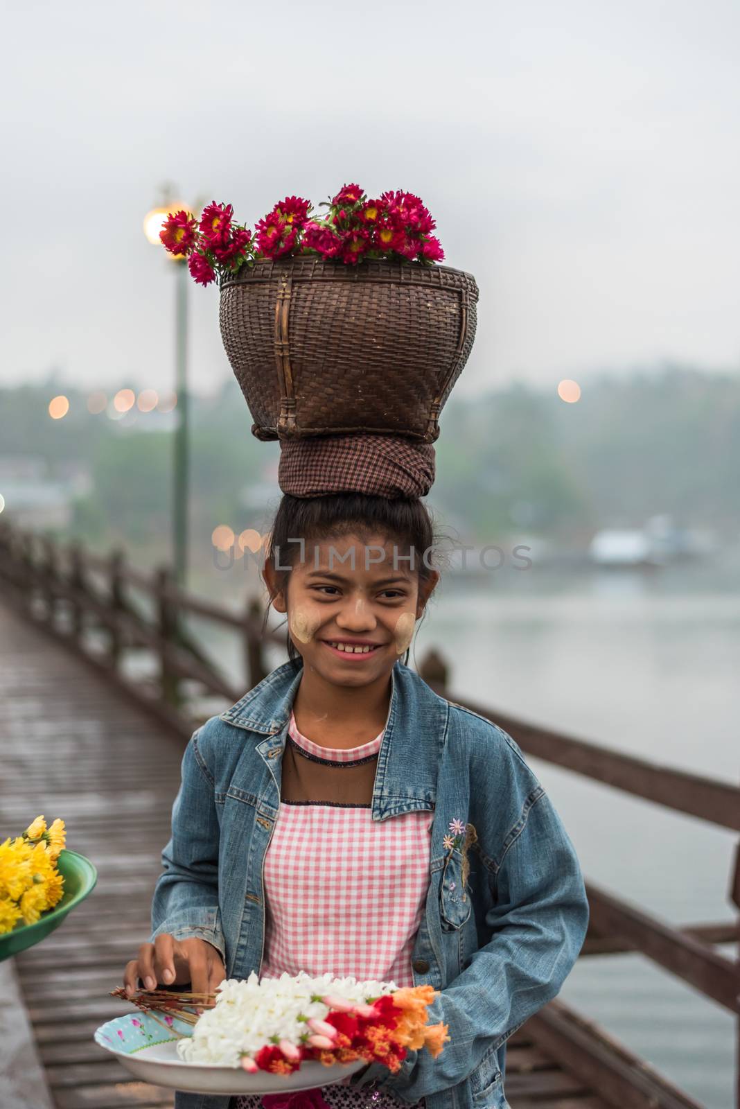 Kanchanaburi, Thailand - March 2, 2018 : Mon woman carry flower basket on the head for transport walking on Mon Bridge, Wooden Bridge in Tambon Nong Lu, Amphoe Sangkhla Buri, Chang Wat Kanchanaburi
