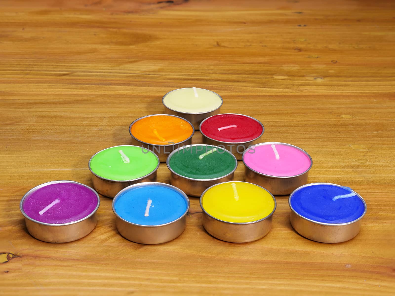 colorful fragrant wax candles arranged in triangular shape to resemble xmax tree, shown on natural wood background