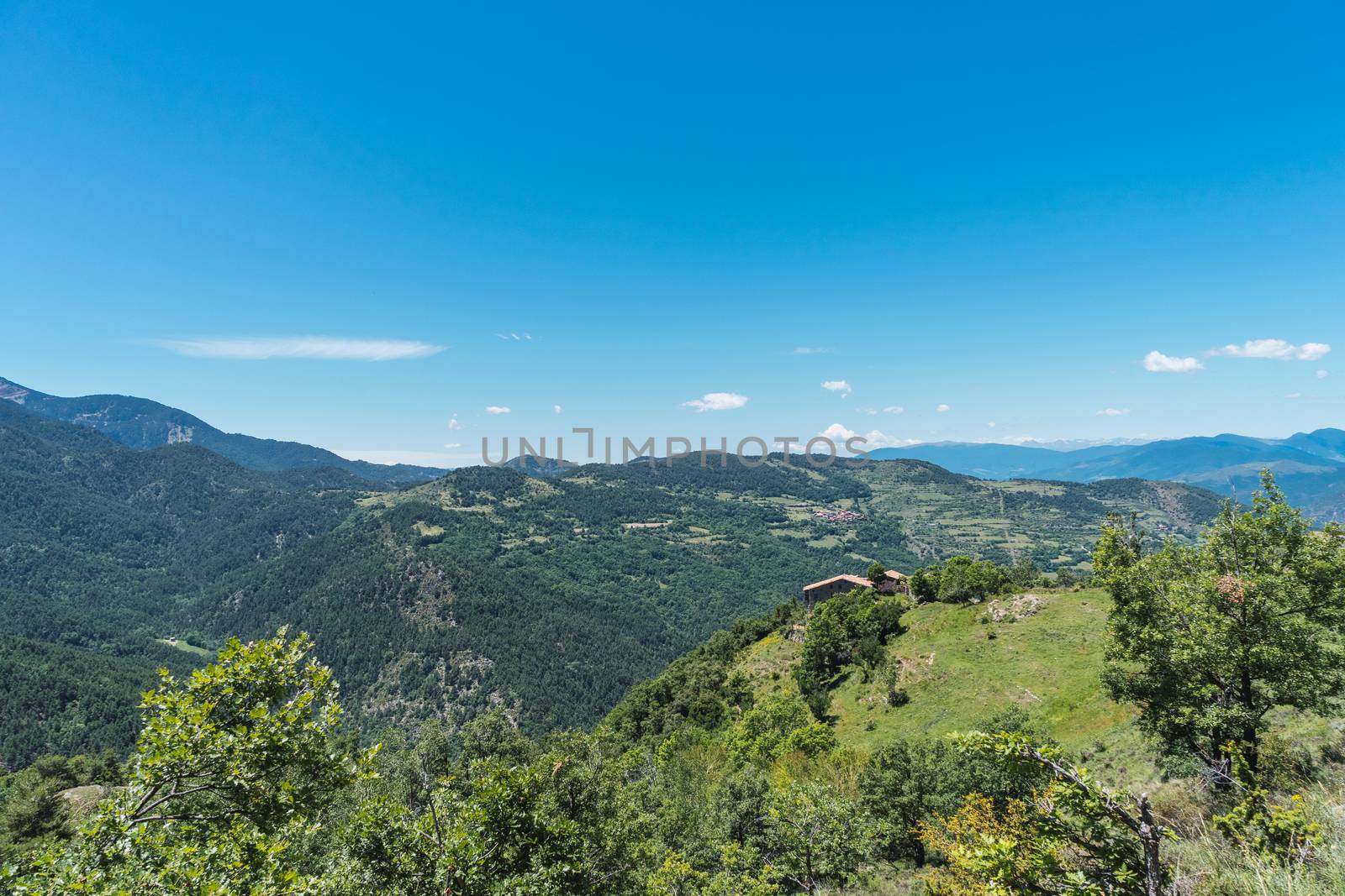 Landscape of the Pyrenees mountains with a farmhouse and a village in the background. Tourism, tranquility, stress-free, peace concept. Connection with nature