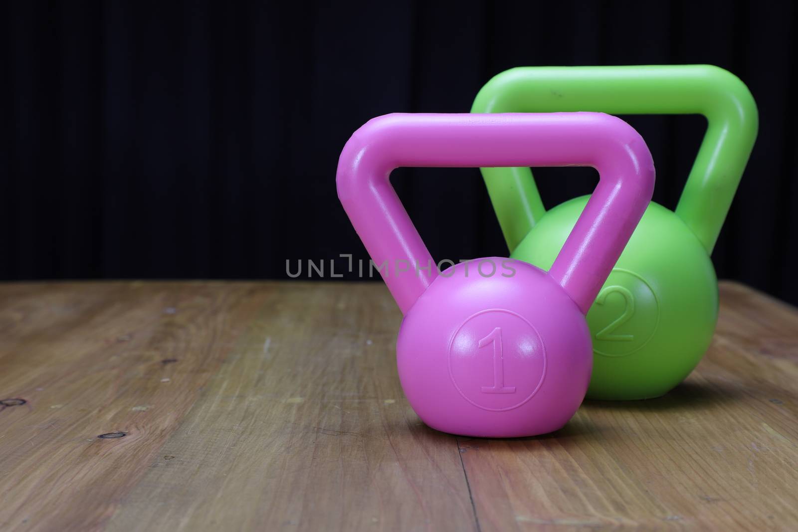 profile view of a green kettlebell for excerising and a large melon on a brown wooden floor