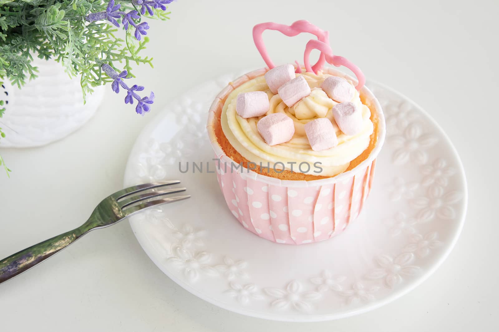A cute cupcake adorned with pink mashmellow and sugar hearts. Top view.
