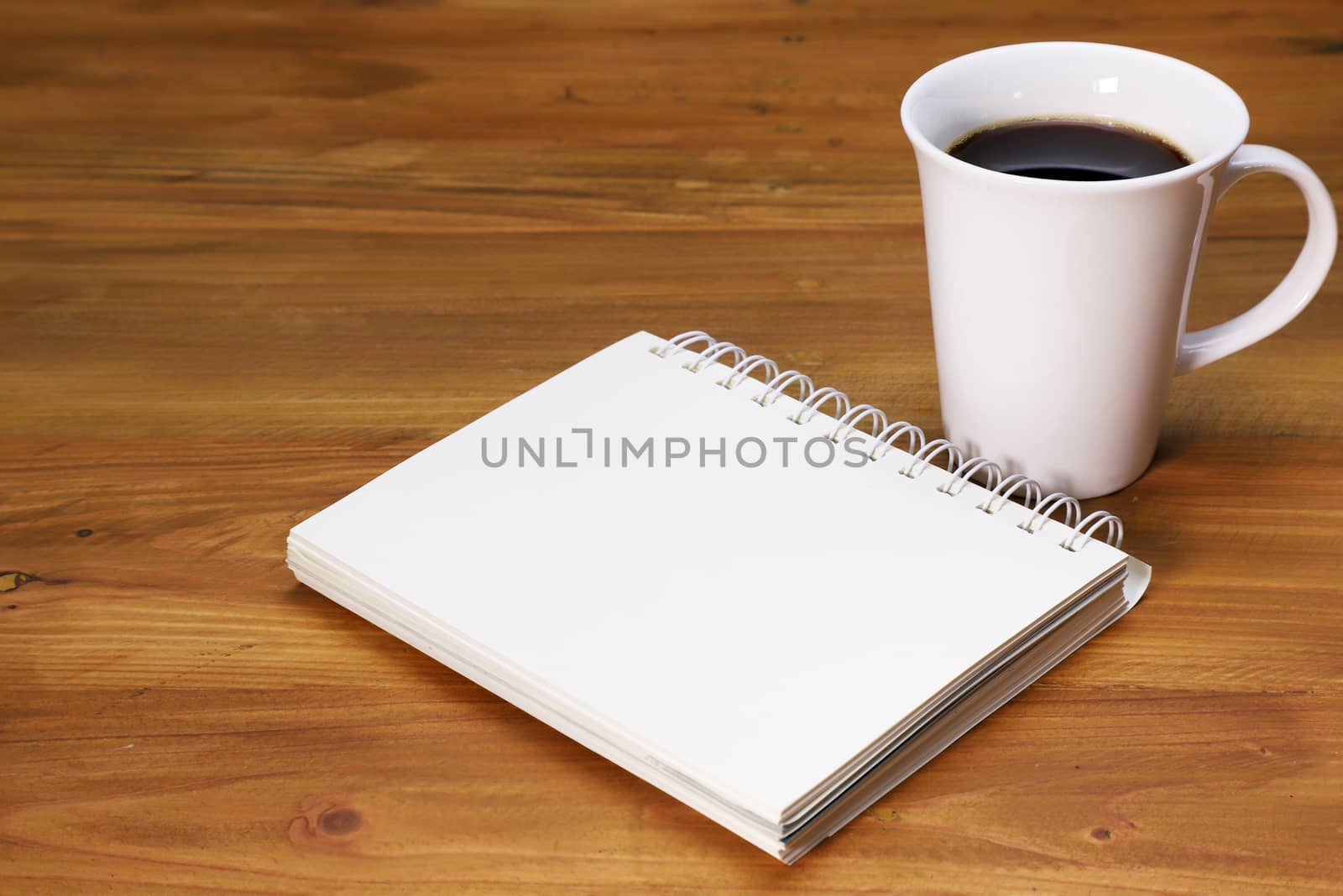 a cup of black coffee and a notebook on a brown wood background