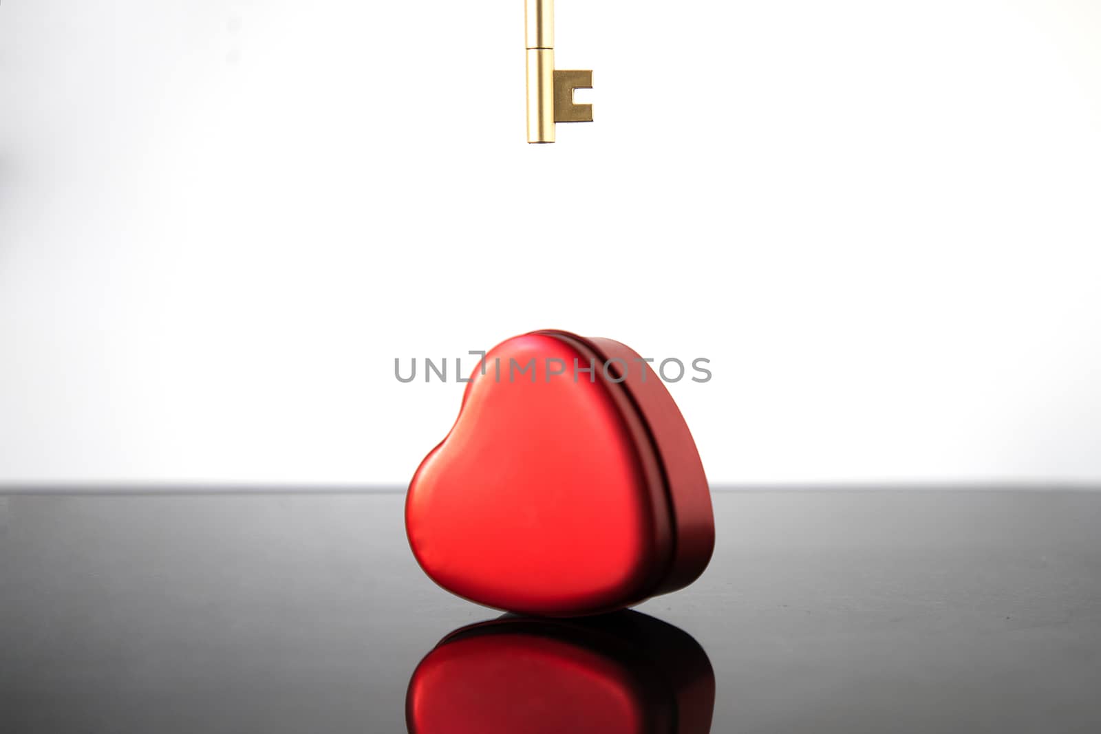 A crimson heart and a gold key on a blurred black and white background. Valentine's Day concept