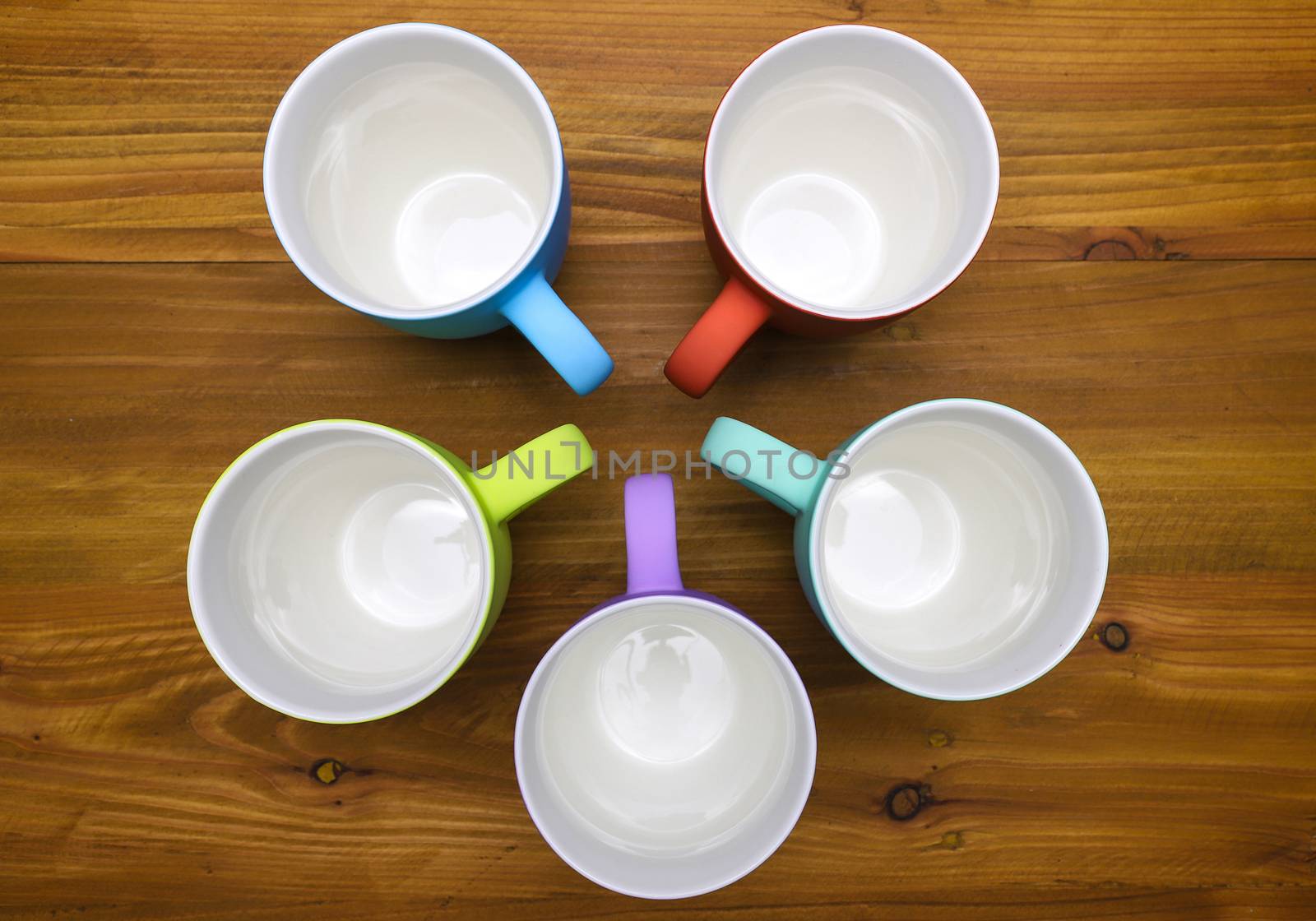 top view of colorful coffee mugs arranged in round pattern, on wooden background