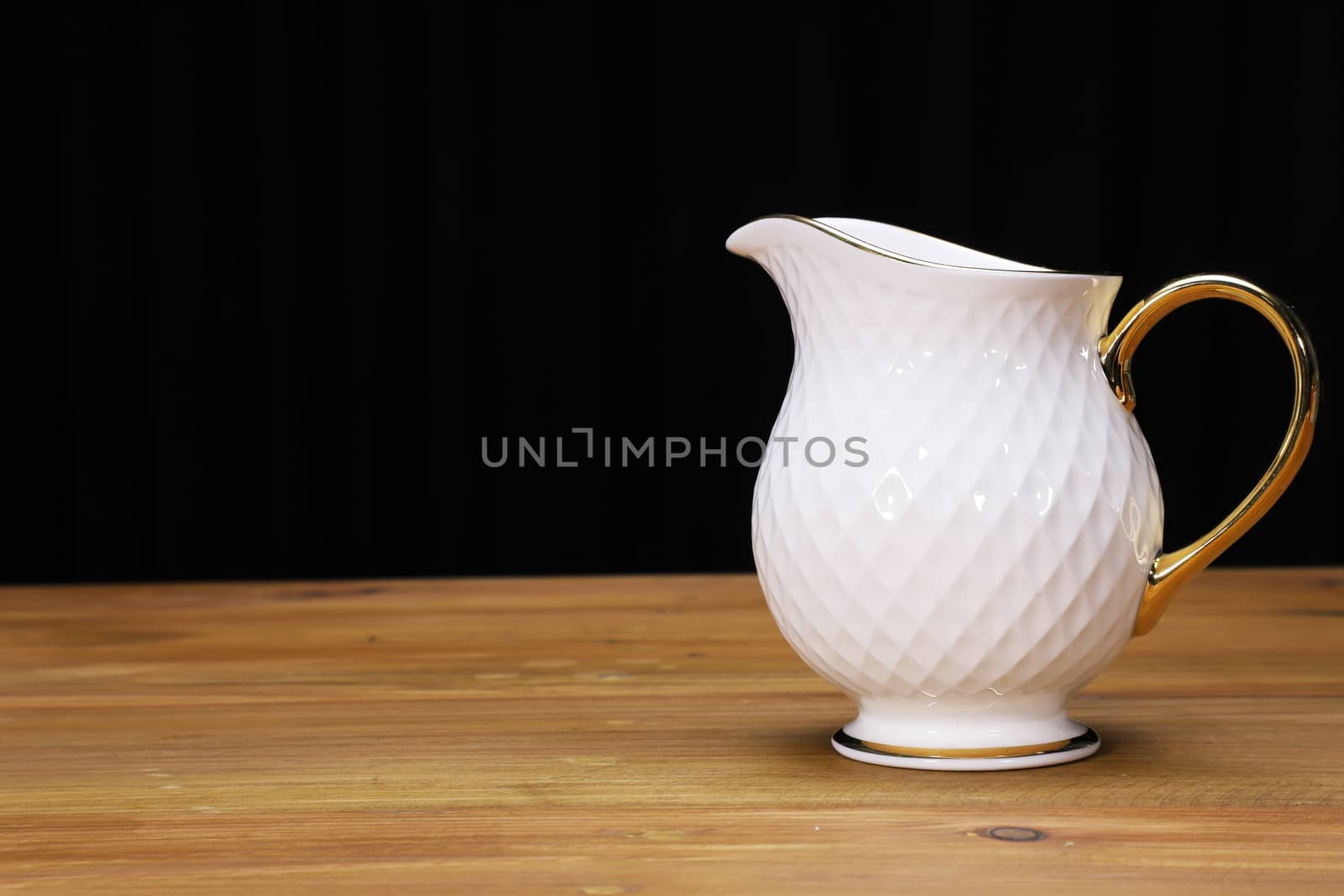 a white porcelain milk jug with gold plated handle on a natural wood table top