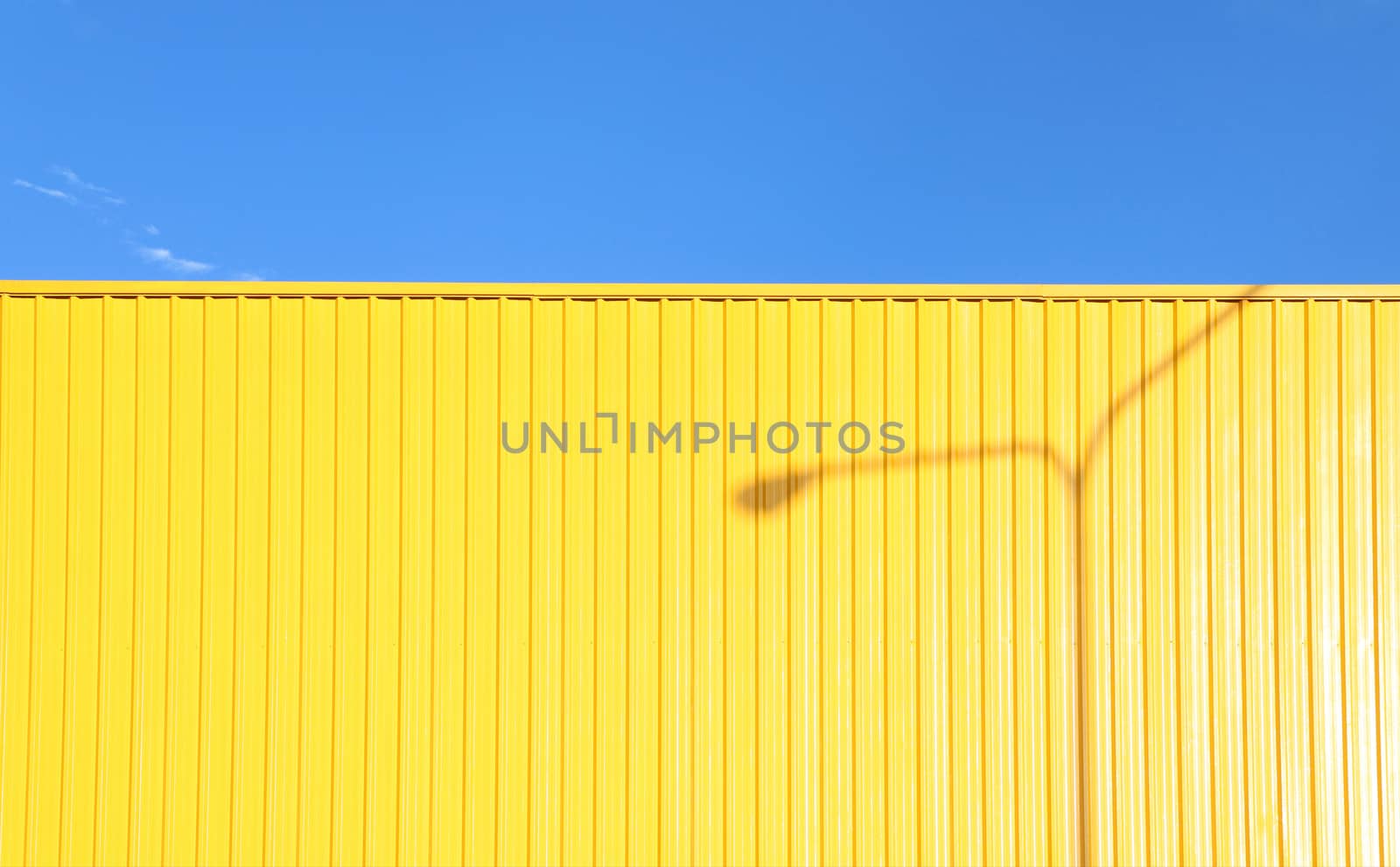 a bright yellow metal wall reflexing the afternoon sun with a shadow of a light pole casting on it