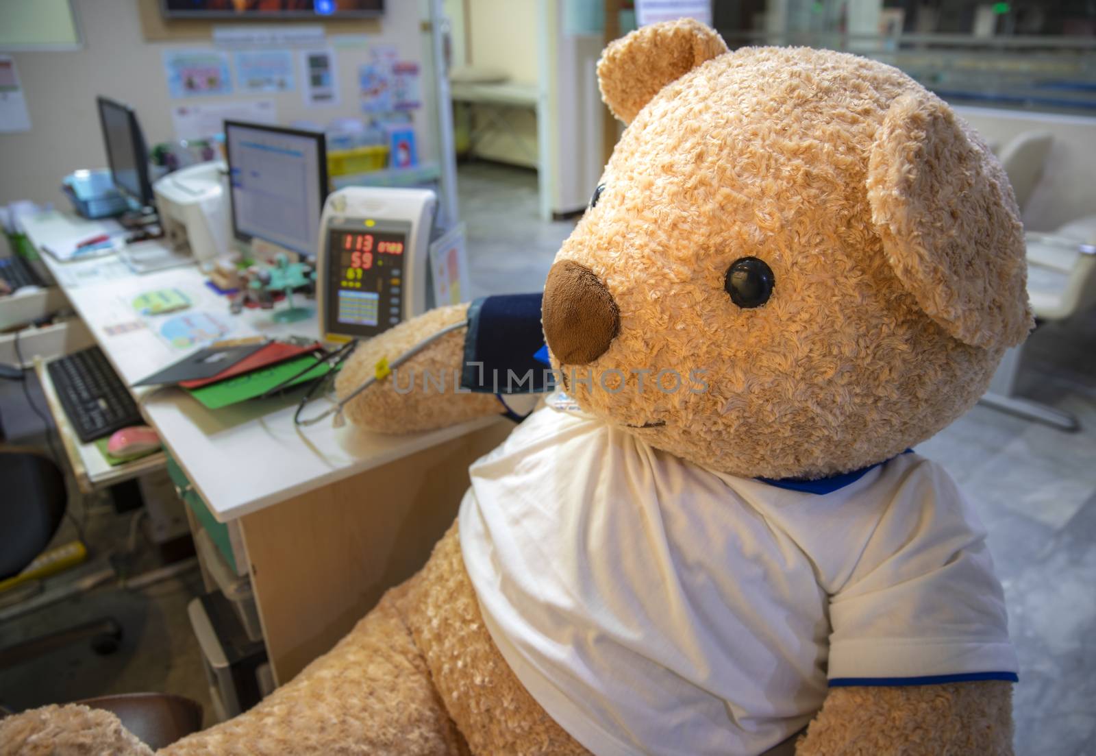A cute live size stuffed toy bear sitting the clinic screening area having blood pressure measured. A campaign aid for children ambulatory clinic.