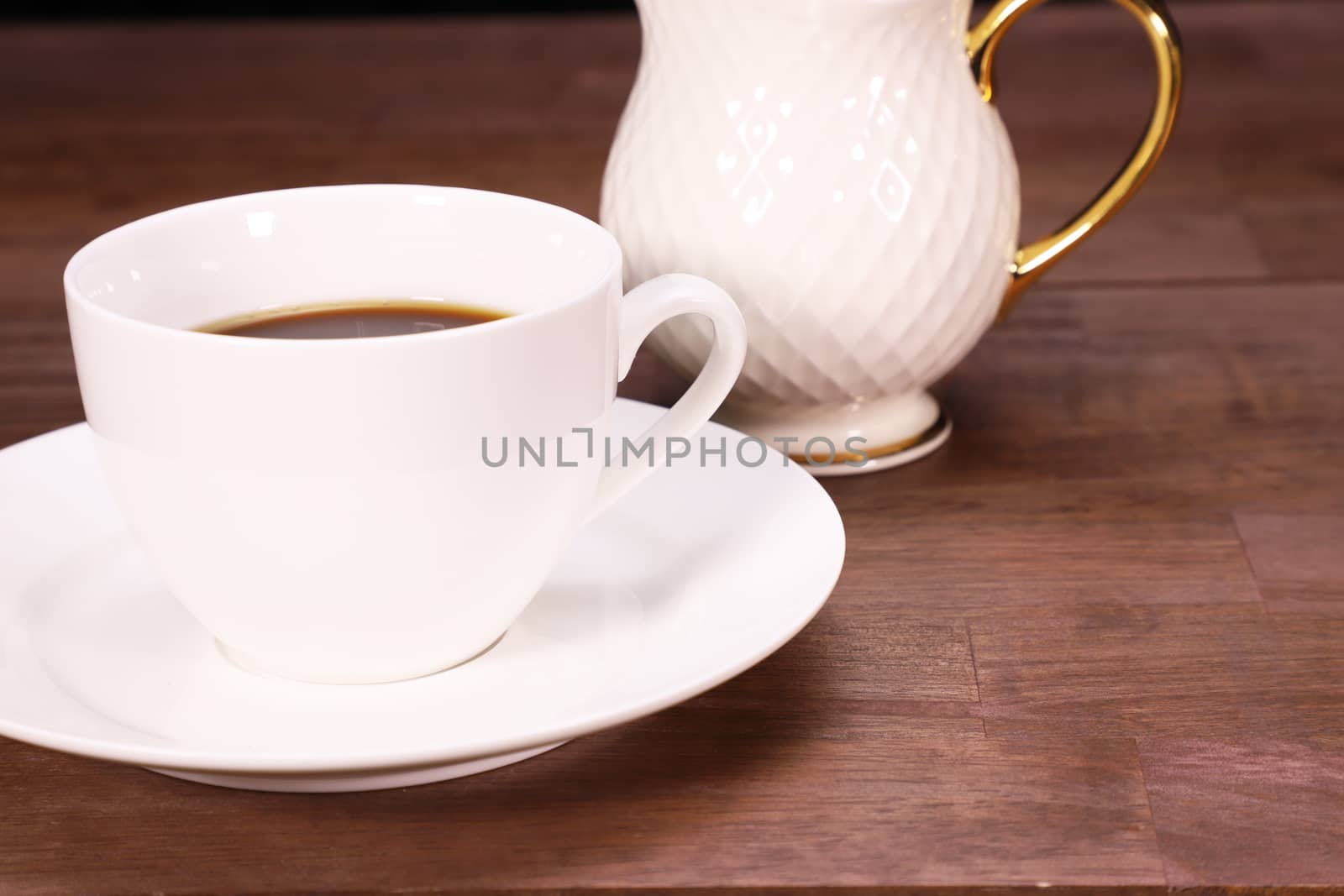 white cup with black coffee on a brown wooden table, with a gold plated bone china milk jug