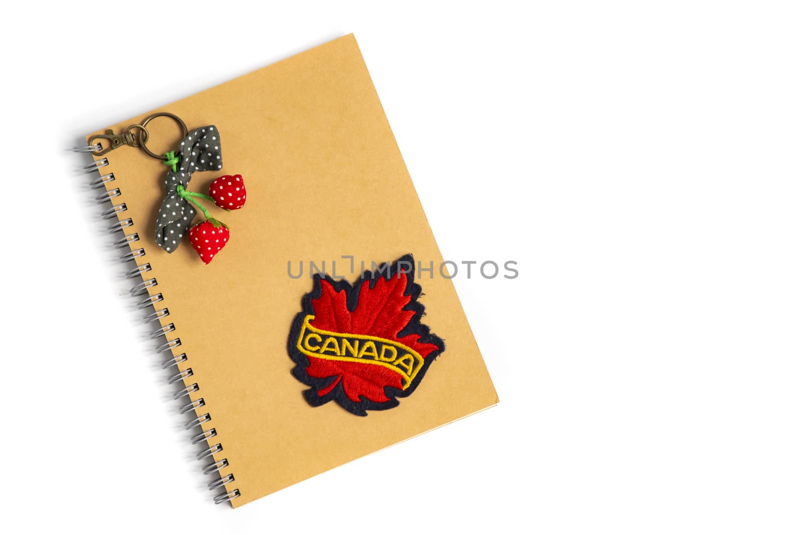A red maple leaf cloth badge with bright yellow Canada text on a brown notebook. Isolated on white background. July 14th, celebration. Happy Canada Day. July 14th.