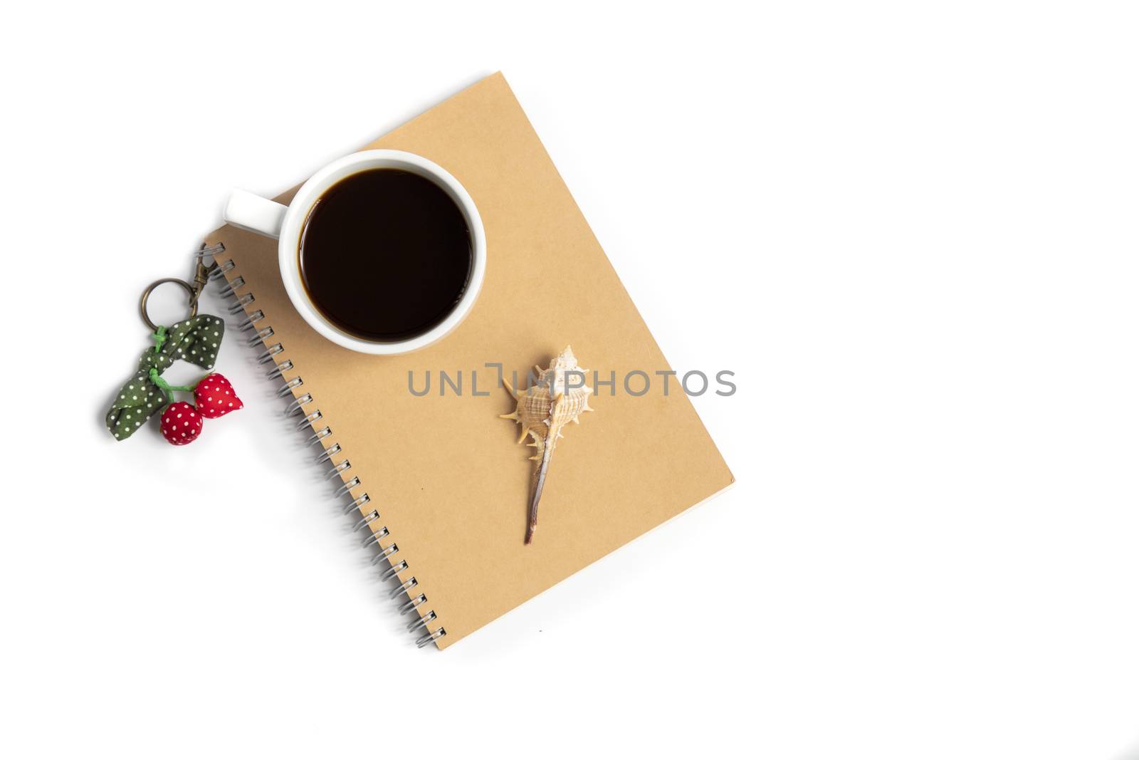 A white cup with black coffee and a seashell with colorful key chain on a brown notebook. Isolated on white background. Summer vacation concepts.