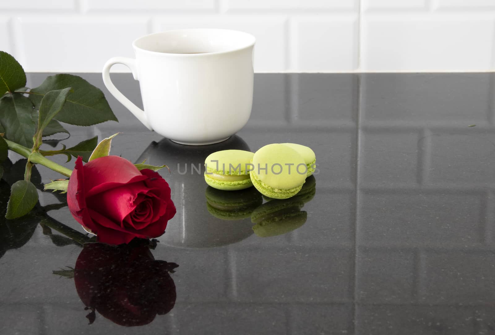 A white ceramic cup with pieces of macarons and a red rose on a black granite kitchen counter.