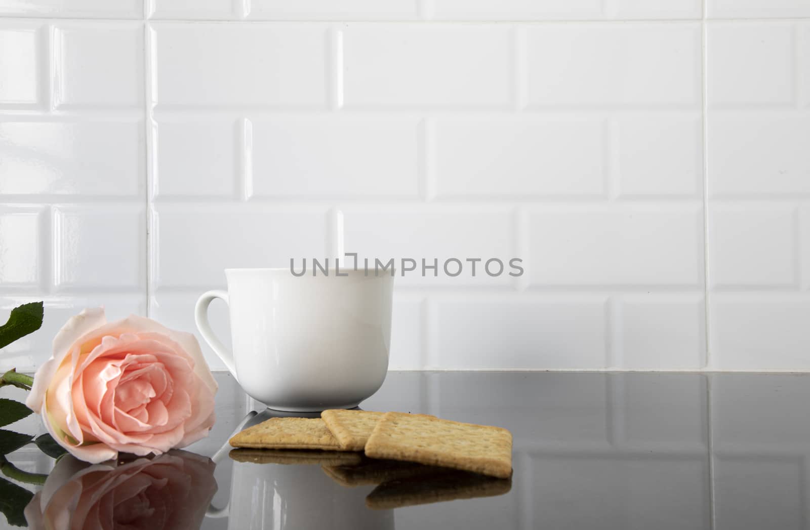 A beautiful peach color rose, pieces of biscute and a white ceramic cup of coffee on a black granite kitchen counter.