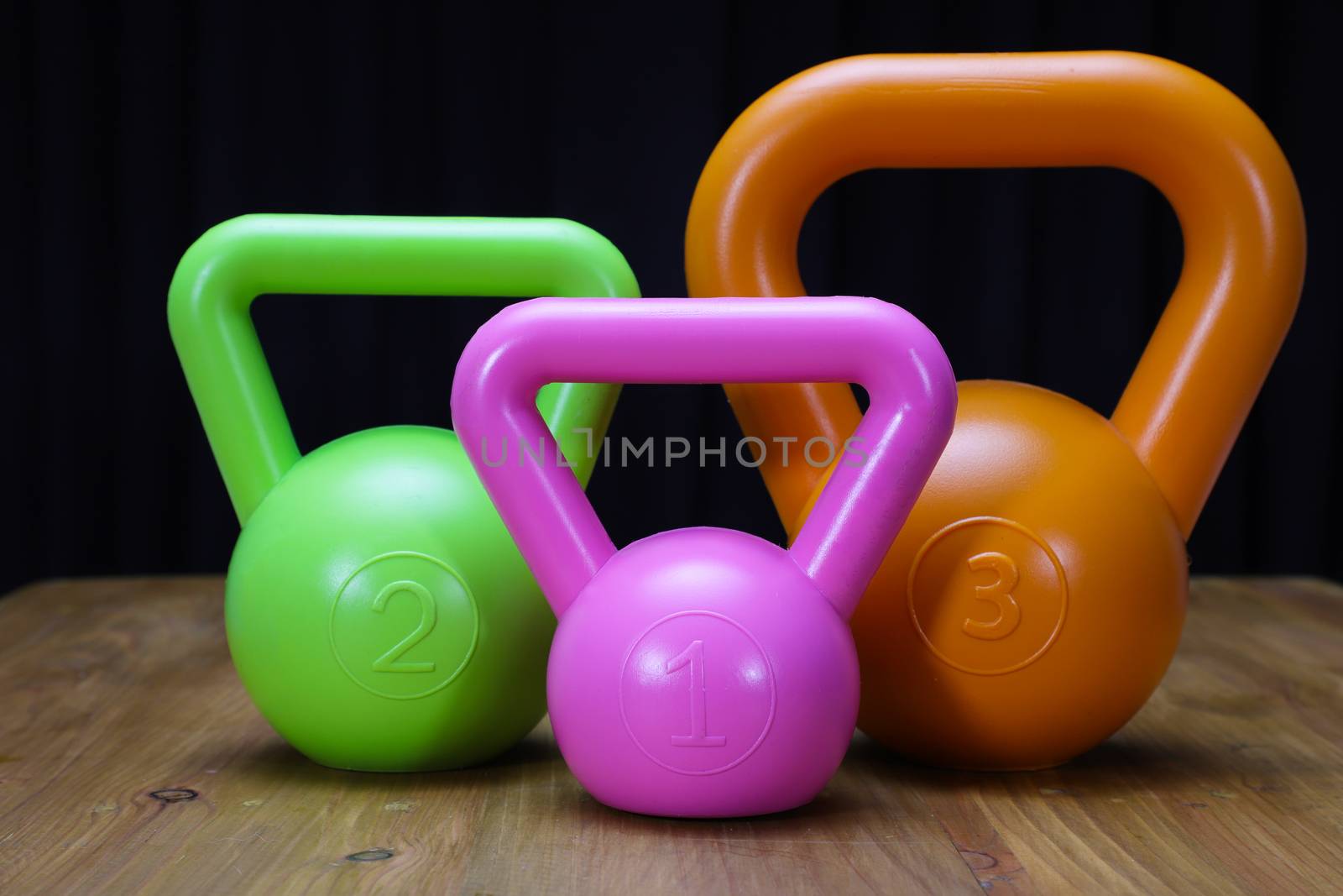 profile view of pink, green, and orange kettlebells on a brown wooden floor