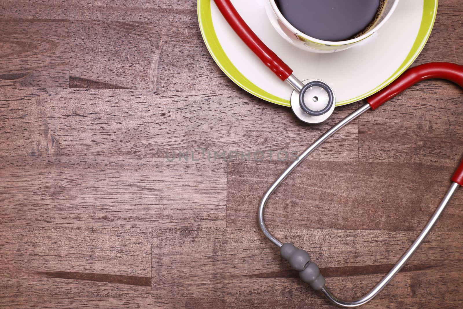 a red stethoscope and a cup of black coffee on a brown table top