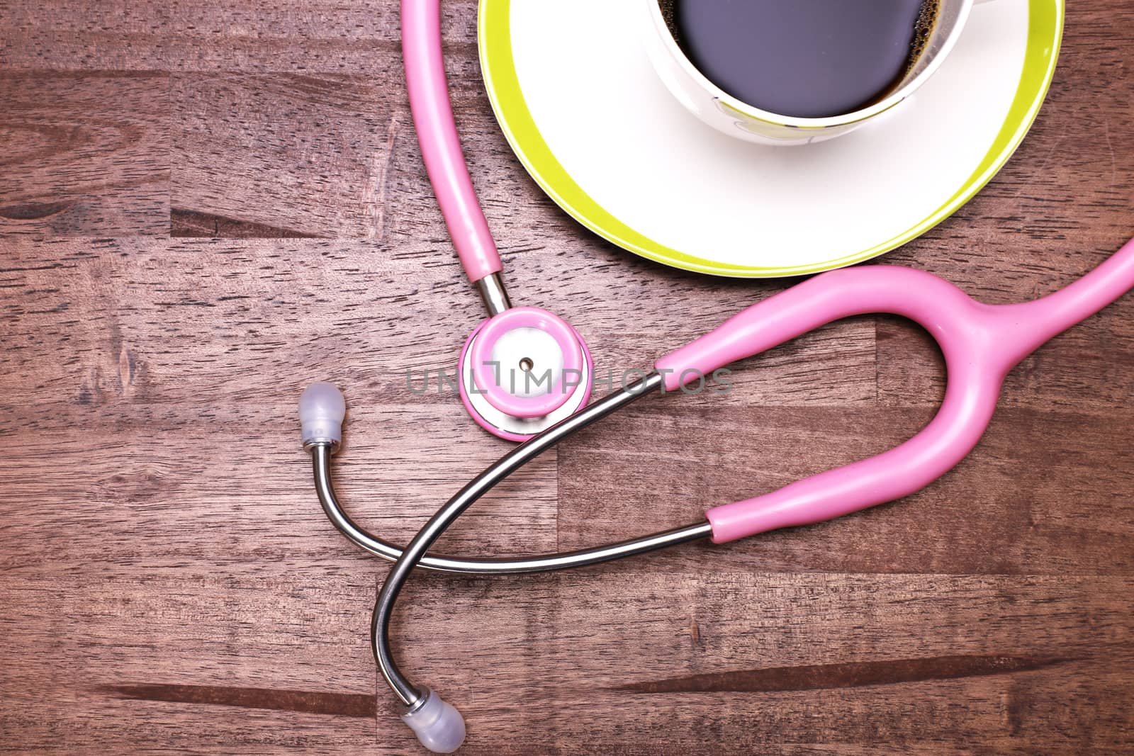 a pink stethoscope and a cup of black coffee on a brown wooden table top