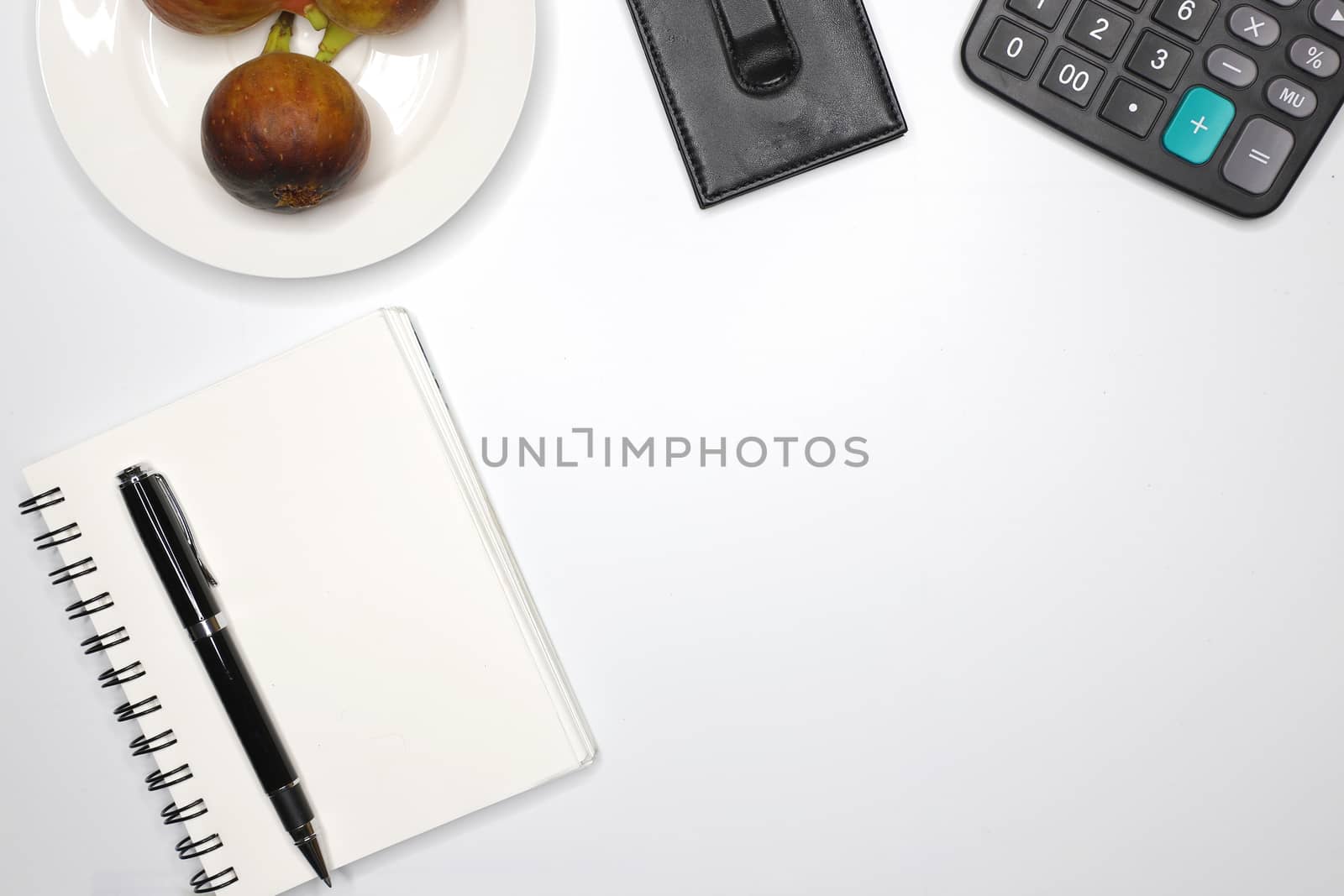 high angle view of a clean business desk top showing a notebook, a black calculator, a black pen, a black wallet, and a fruit plate