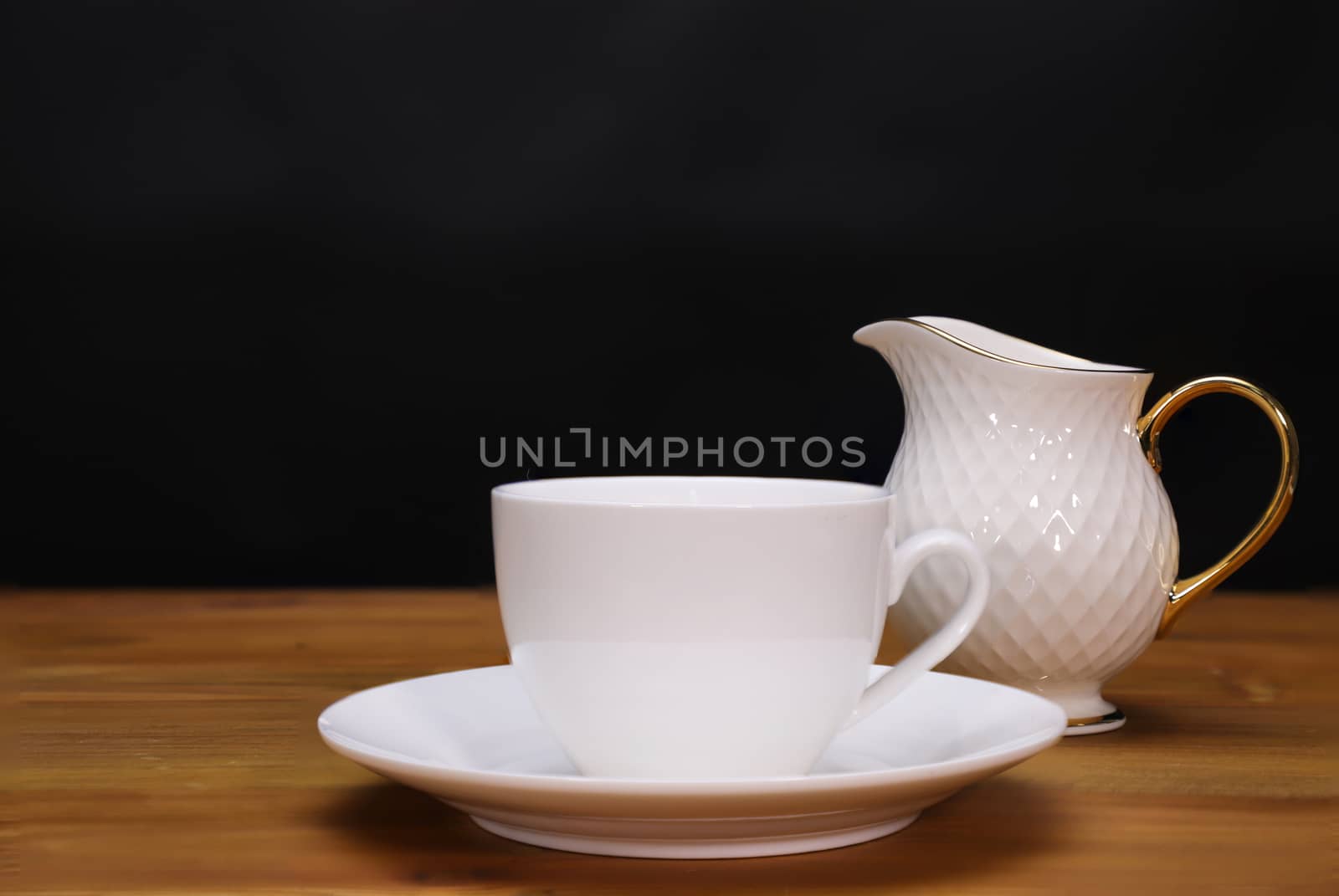 coffee cup, saucer, and milk jug, on wooden table top, black background