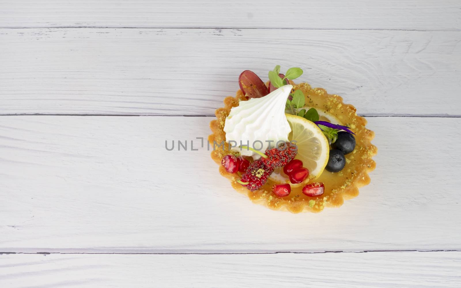 Lemon tart and fresh mixed fruits . Closeup, on creamy white wooden background.