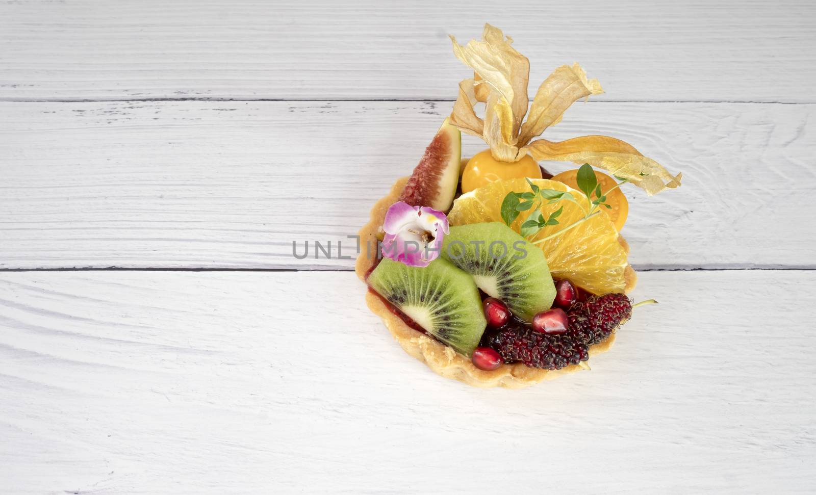 Lemon tart with raspberry jam and fresh mixed fruits . Closeup, on creamy white wooden background.