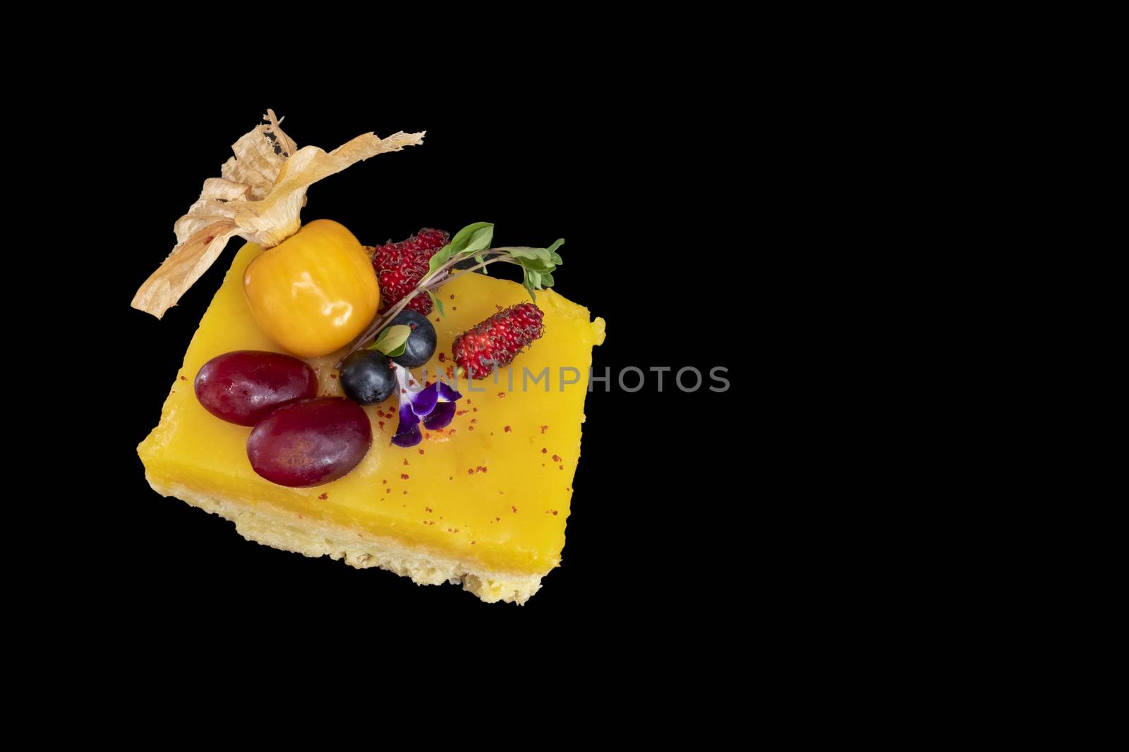 A piece of colorful lemon custard shortbread with fresh mixed fruits isolated on dark black background. Closeup top view.