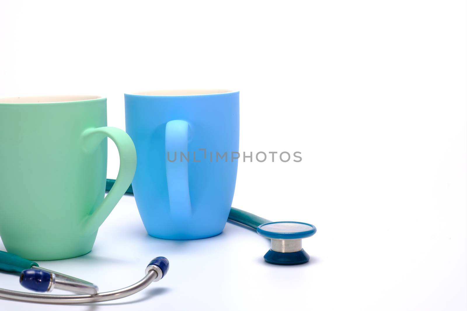a green stethoscope and two colorful coffee mugs on white background
