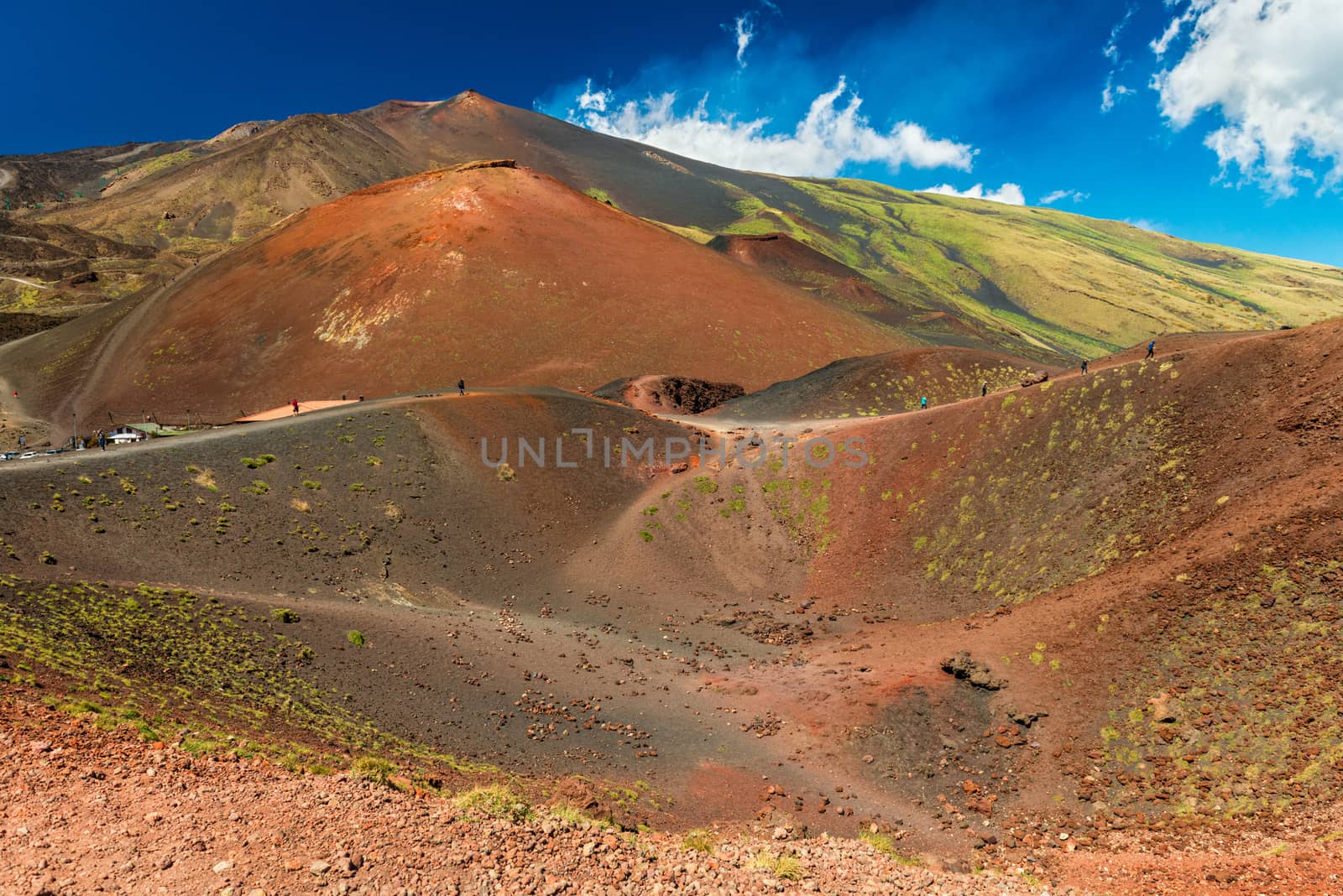 Beautiful landscape with lava hills covered with grass, a volcanic crater and people walking around it. Mount Etna, Sicily, Italy