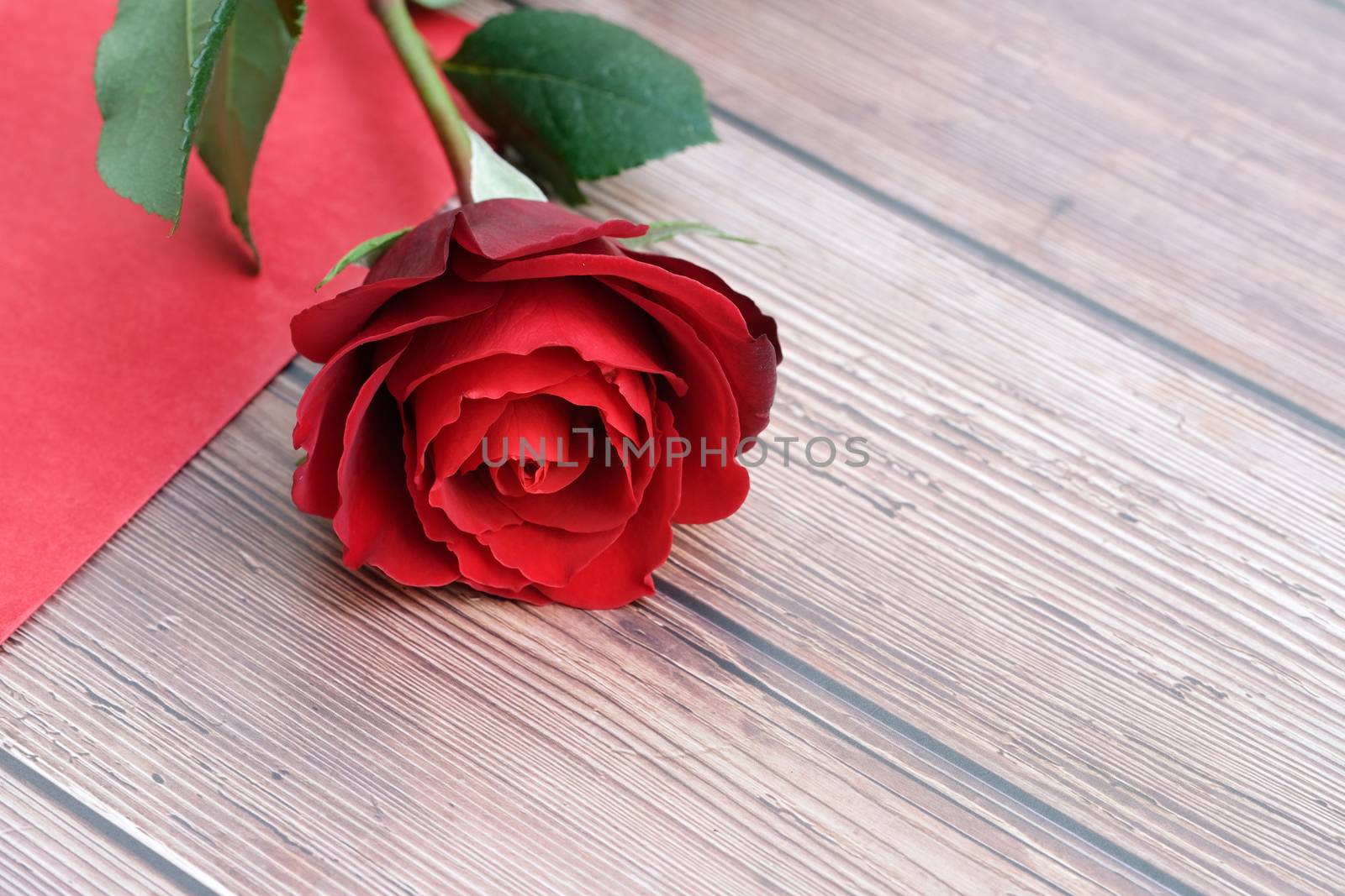 A single beautiful red rose and an envelope on a brown wooden background.