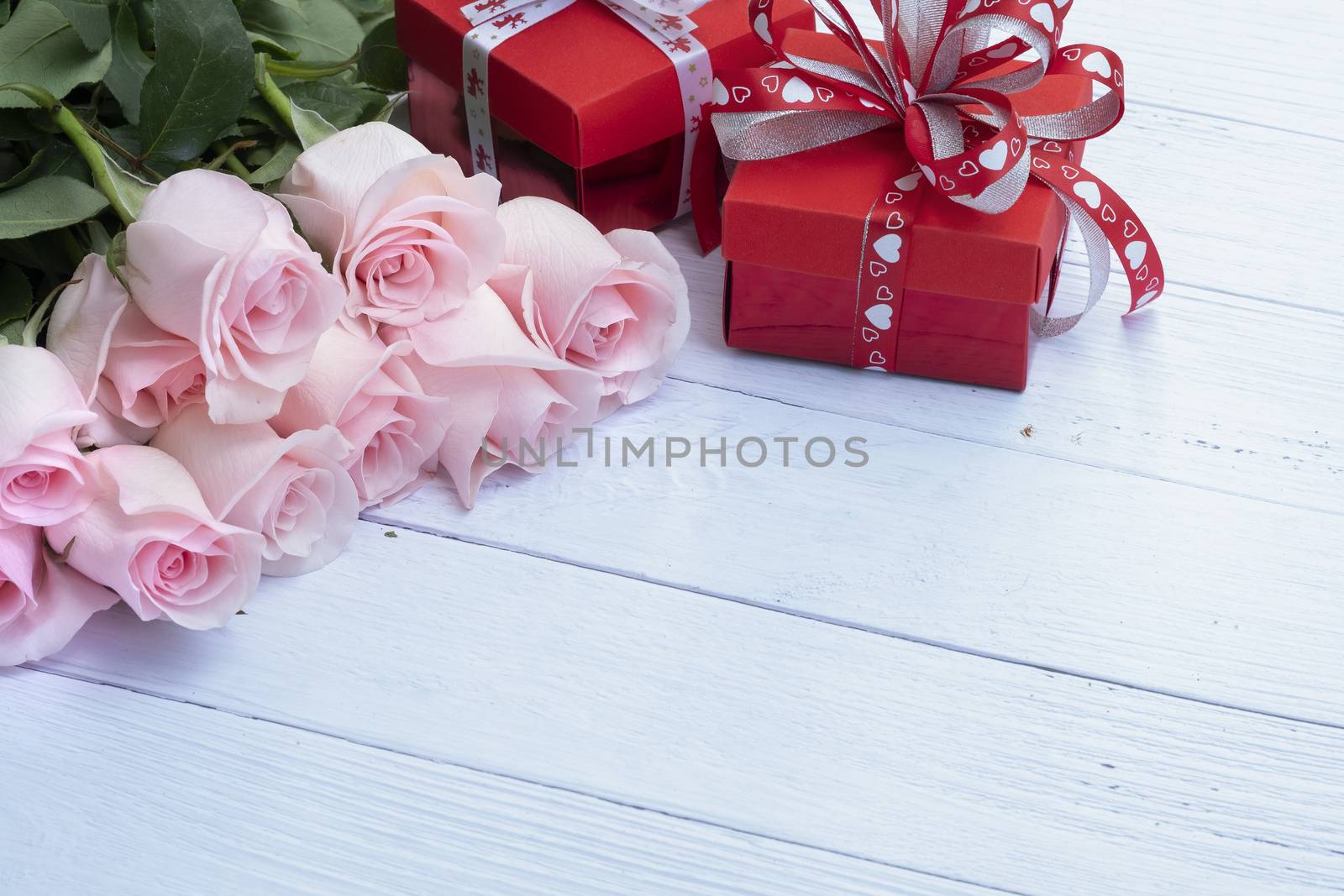 Beautiful bouquet of pink roses and red present boxes on pale blue-colored wood background. Selective focusing. Love, Romance, Valentine's Day, Anniversary.