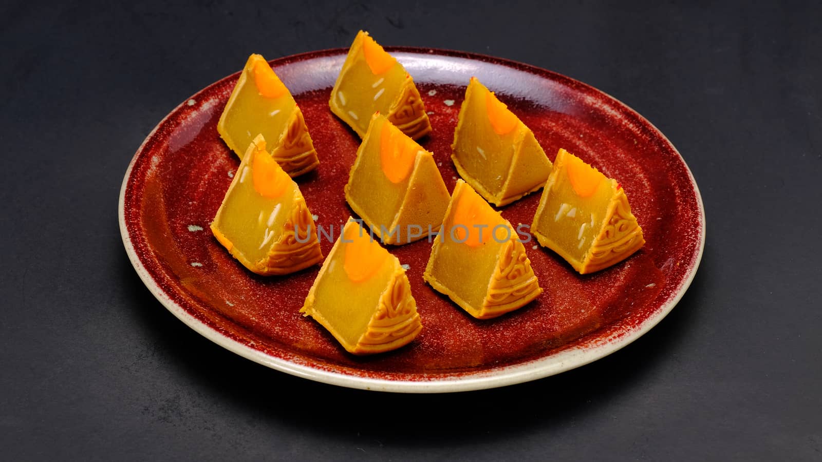 moon-cake, a traditional chinese pastry, eaten during the harvest moon festival in october, is composed of durian, sweet bean and almond slices fillings, with preserved duck york in the center, is placed on a red cceramic plate