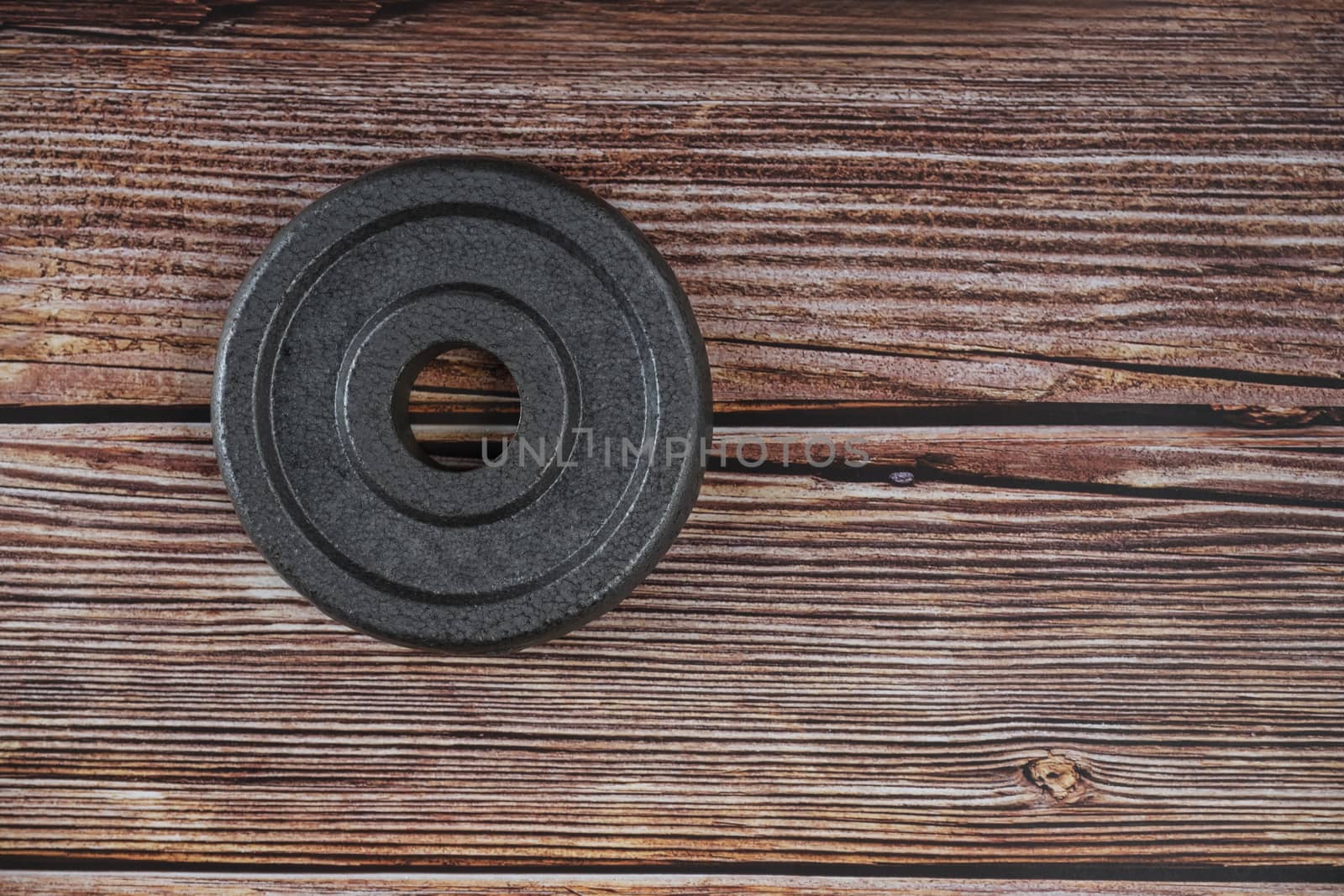 A metal weight plate on brown wooden background.