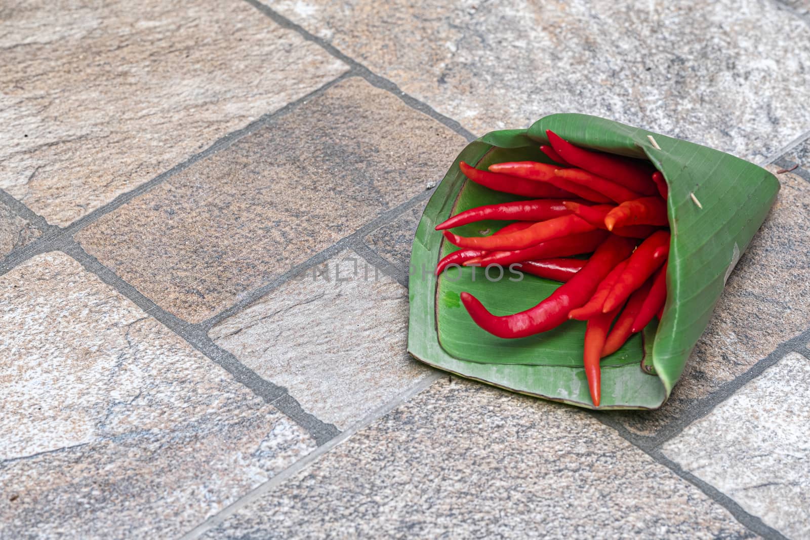 A bunch of red hot chilli peppers covered with traditional northern thai banana leaf container on concrete floor background.