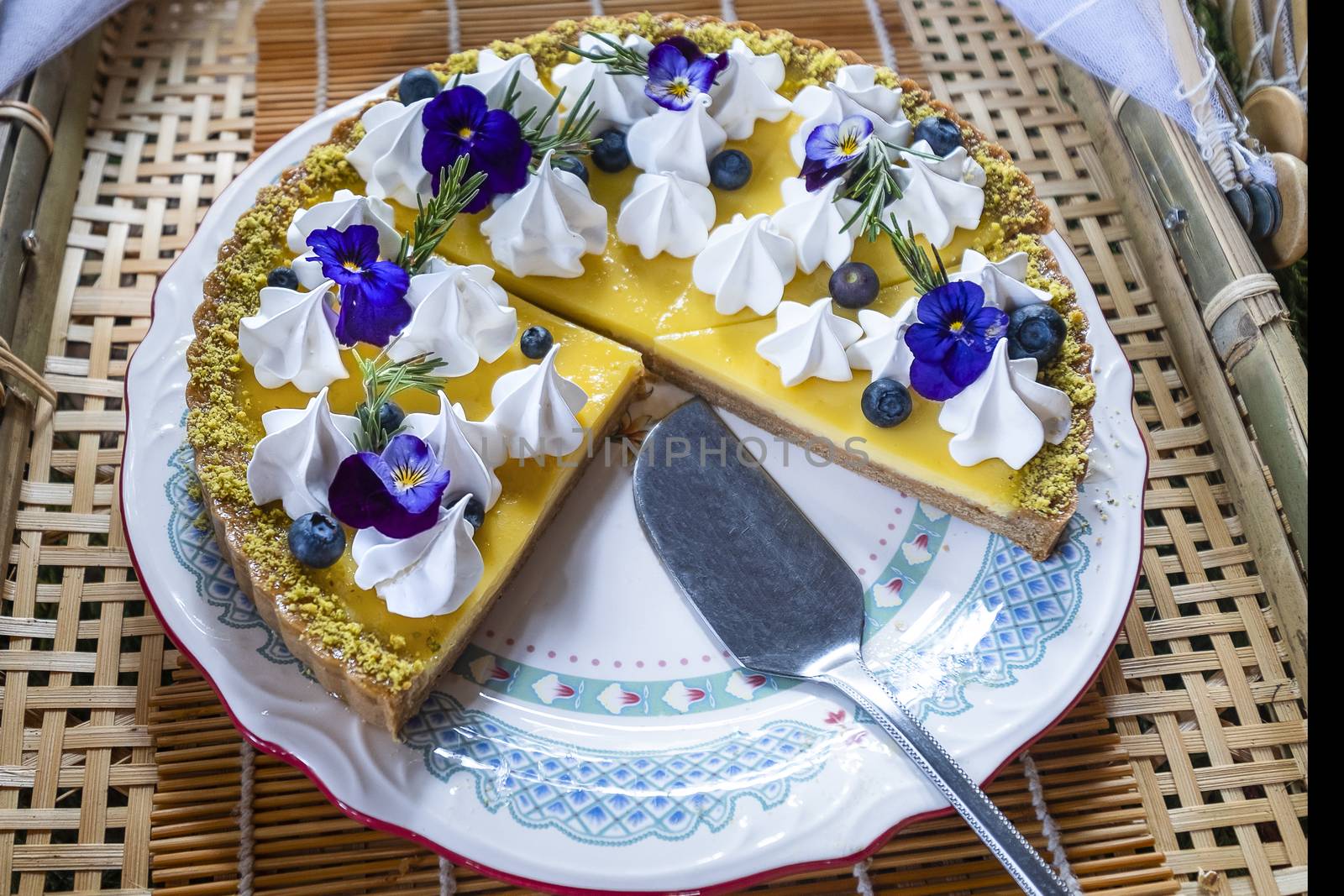 Homemade lemon pie topped with creamy white meringue, blueberries, rosemary sprigs and blue flowers. Rustic background.