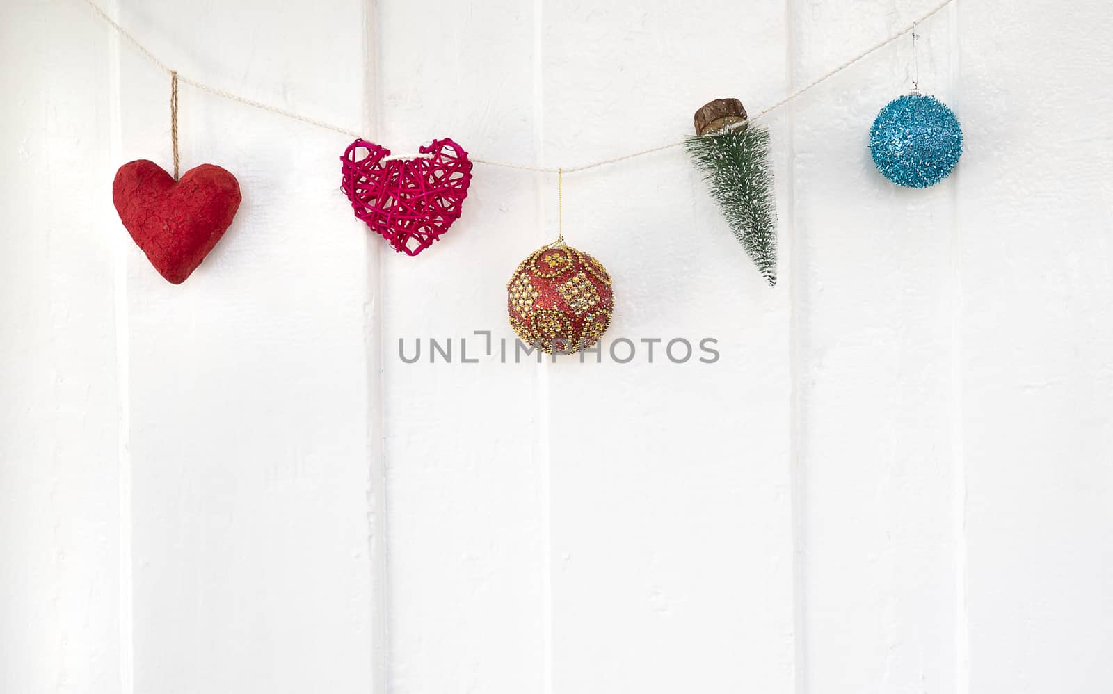 Christmas ornaments hanging on a white strng on a white wooden wall of a home. Minimal holidays decoration.