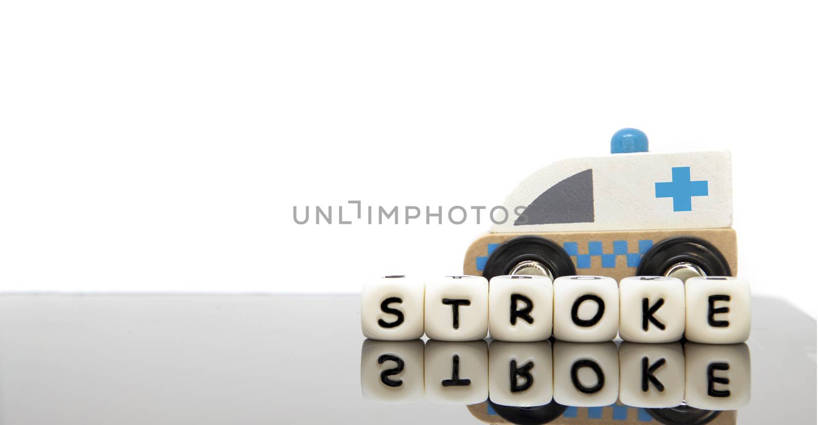 Alphabet letters spelling the word stroke and a wooden toy ambulance. White background. Emergency medicine concept.