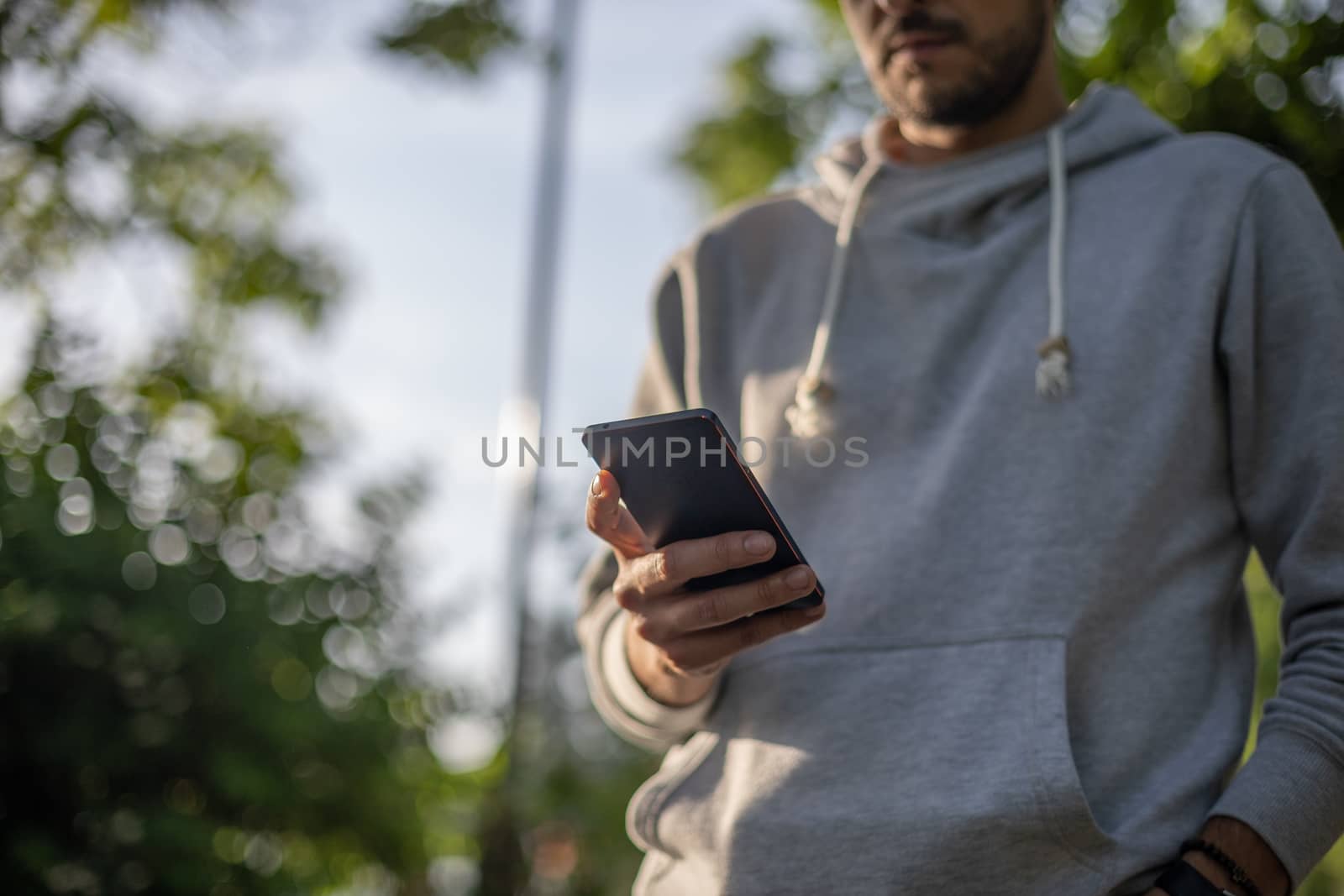 Man texting message on smartphone, outdoor park shoot, back light