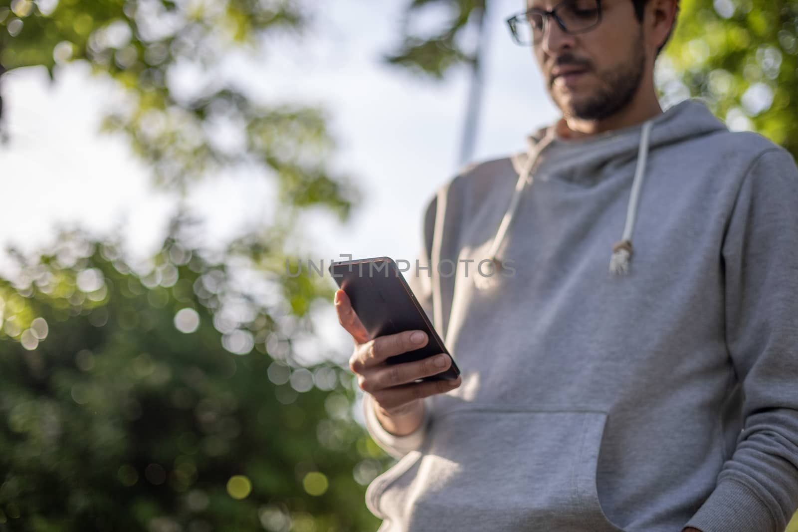 Smart looking man texting message on smartphone, outdoor park shoot, back light