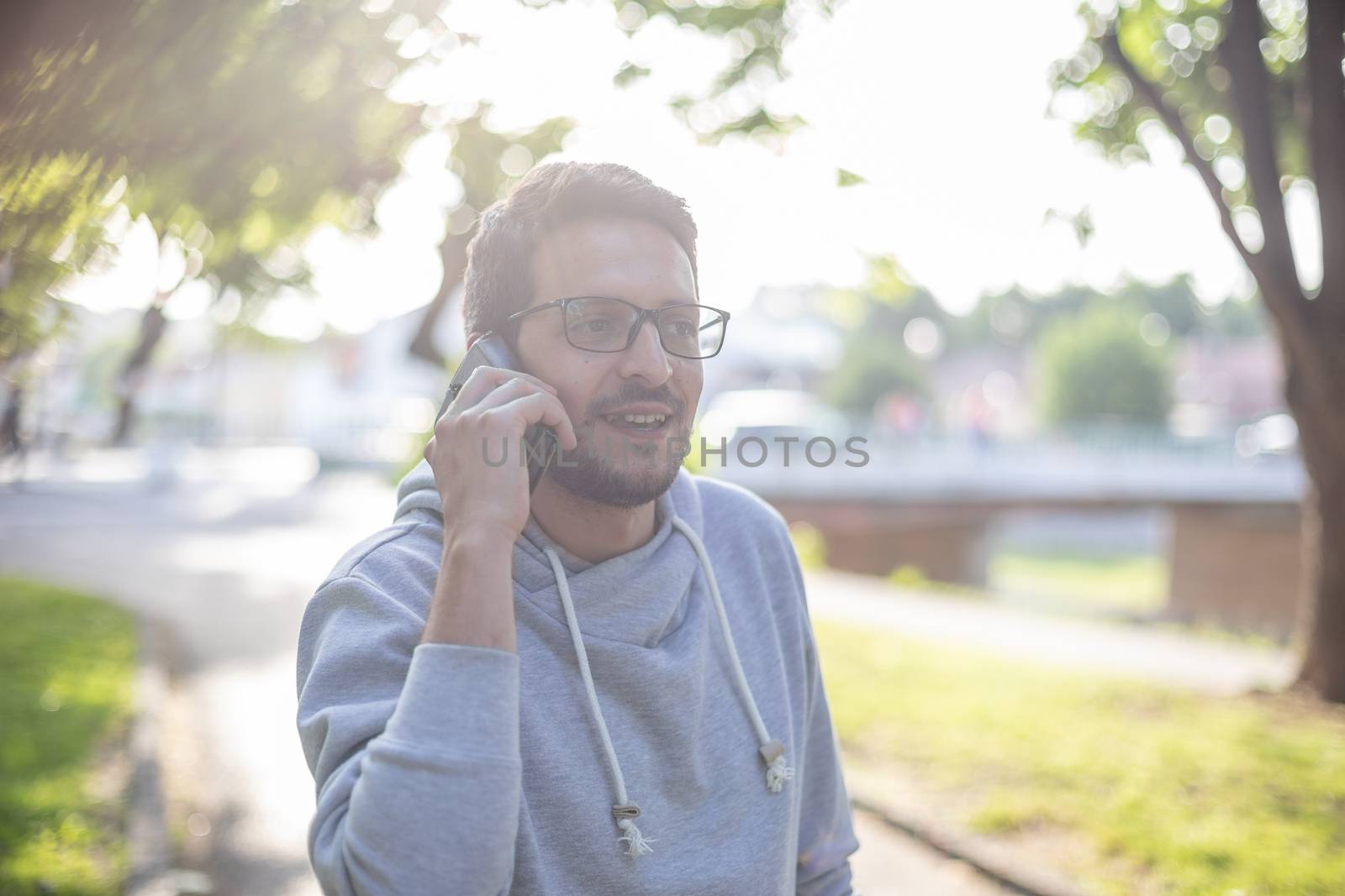 Good news and happy face - Man talking on smartphone in park, outdoor shoot, back light