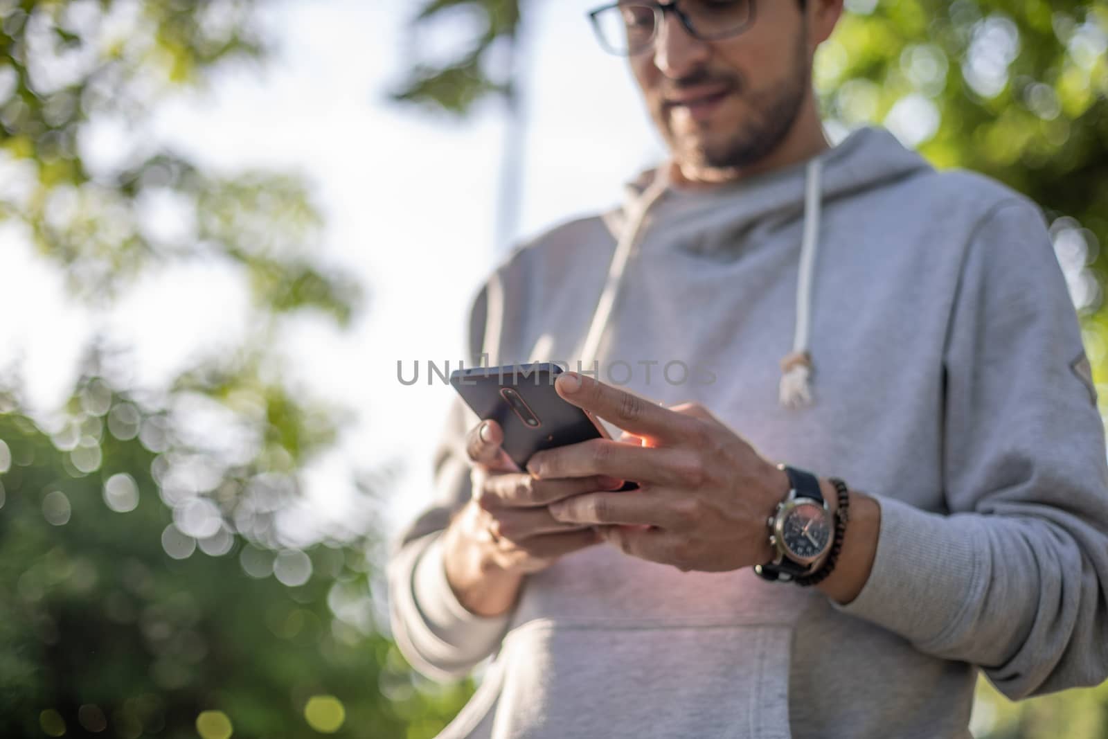 Smart looking man texting message on smartphone in park, back li by adamr