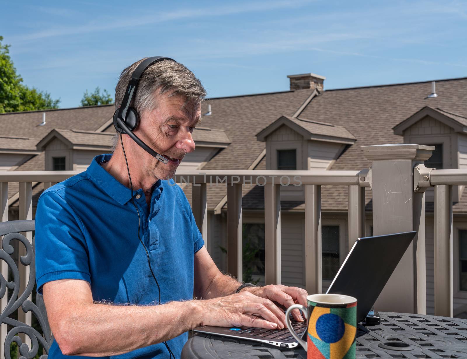 Senior man working from home on outdoor deck with headset and computer by steheap