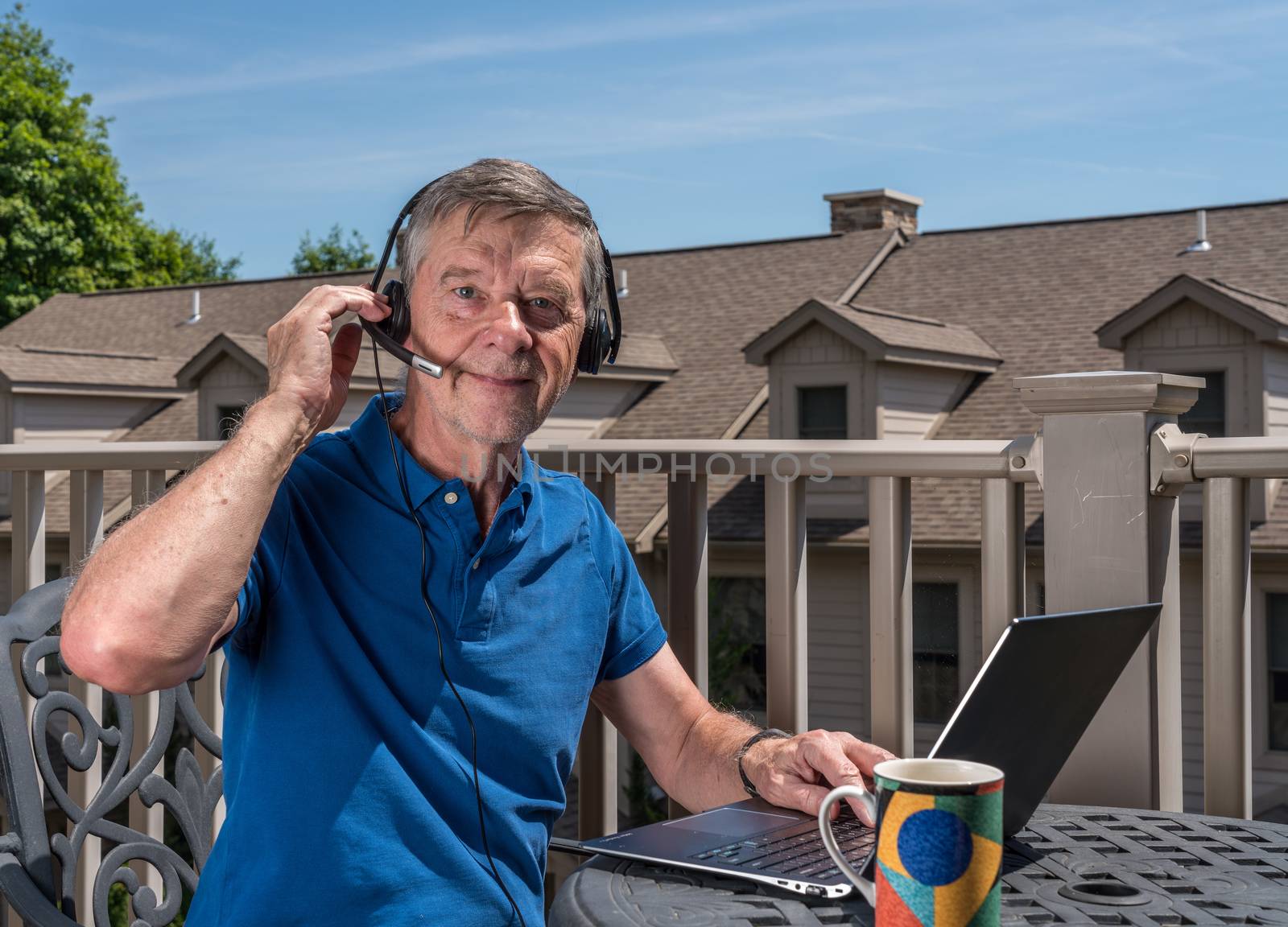 Senior man working from home on outdoor deck with headset and computer by steheap