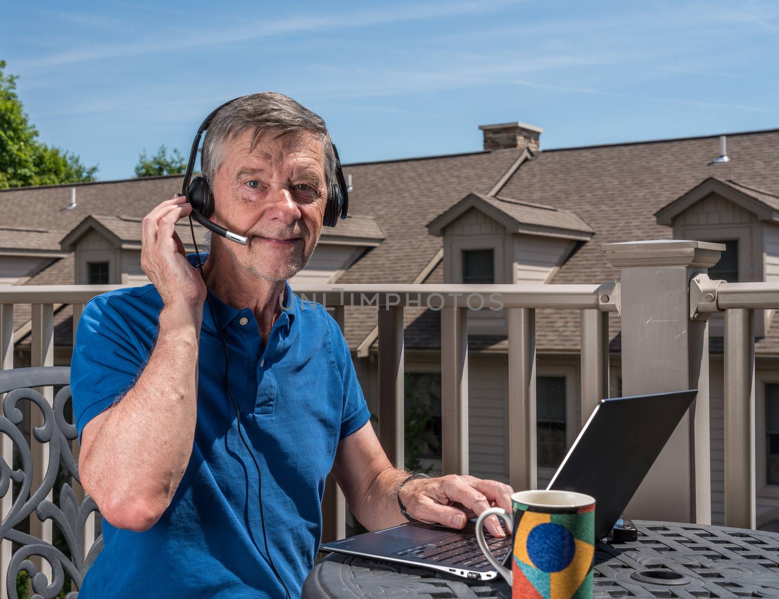 Senior man working from home on outdoor deck with headset and computer by steheap