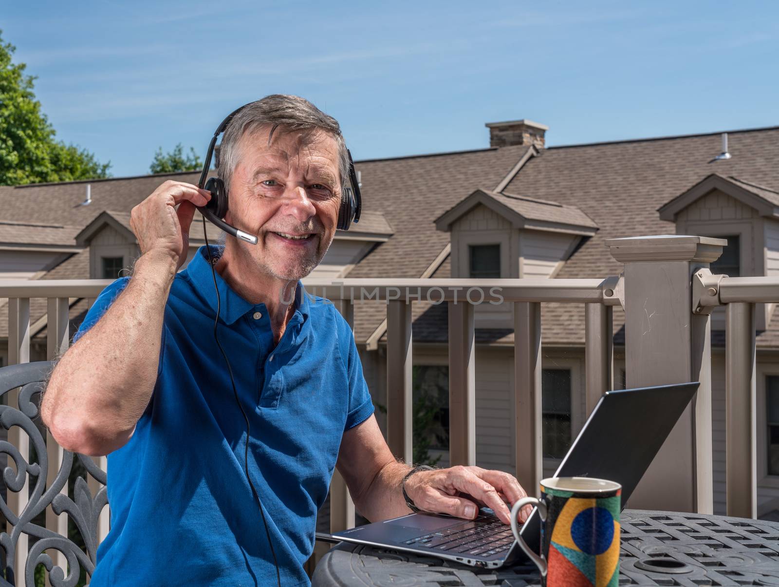 Senior man working from home on outdoor deck with headset and computer by steheap
