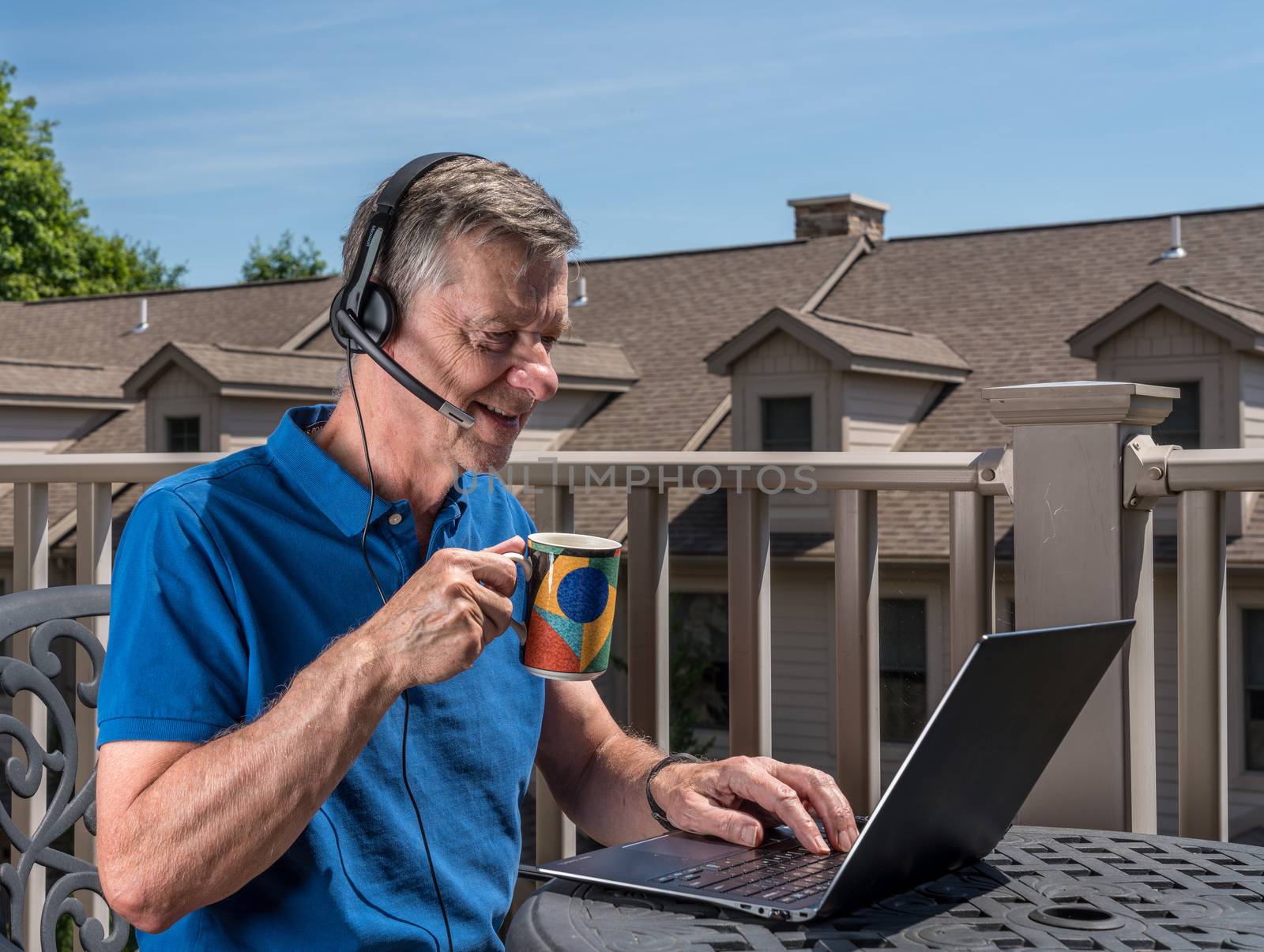 Senior man working from home on outdoor deck with headset and computer by steheap