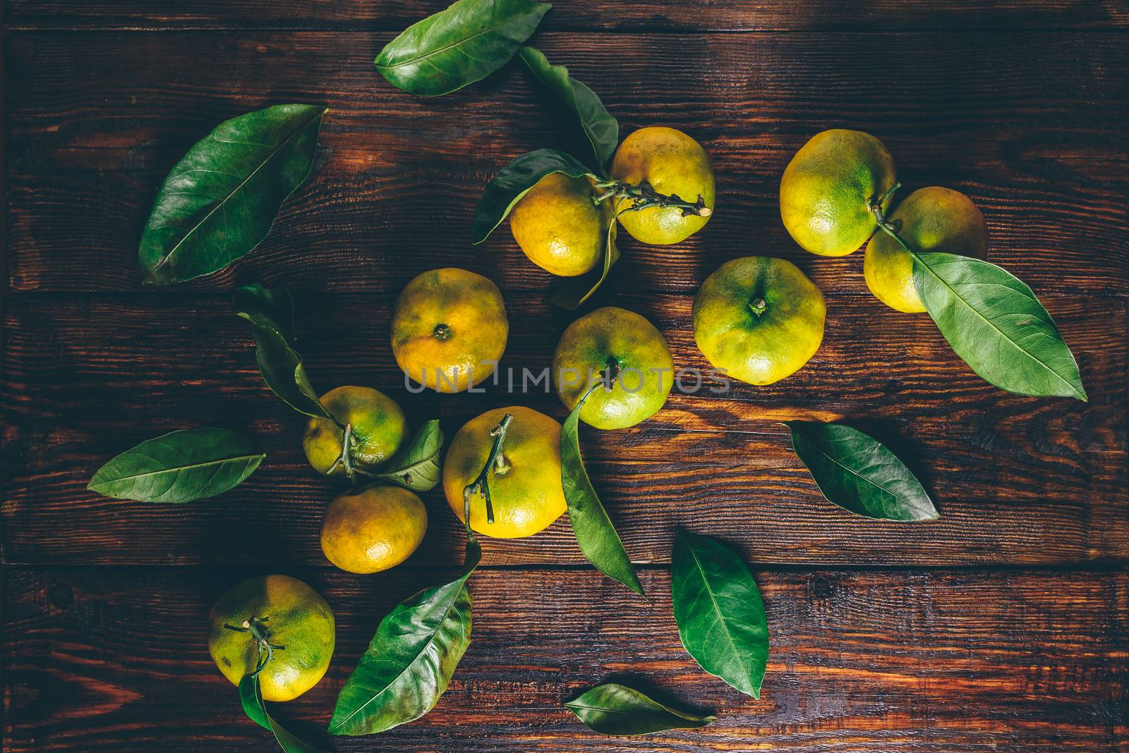 Yellow-green tangerines with leaves over wooden surface. View from above.