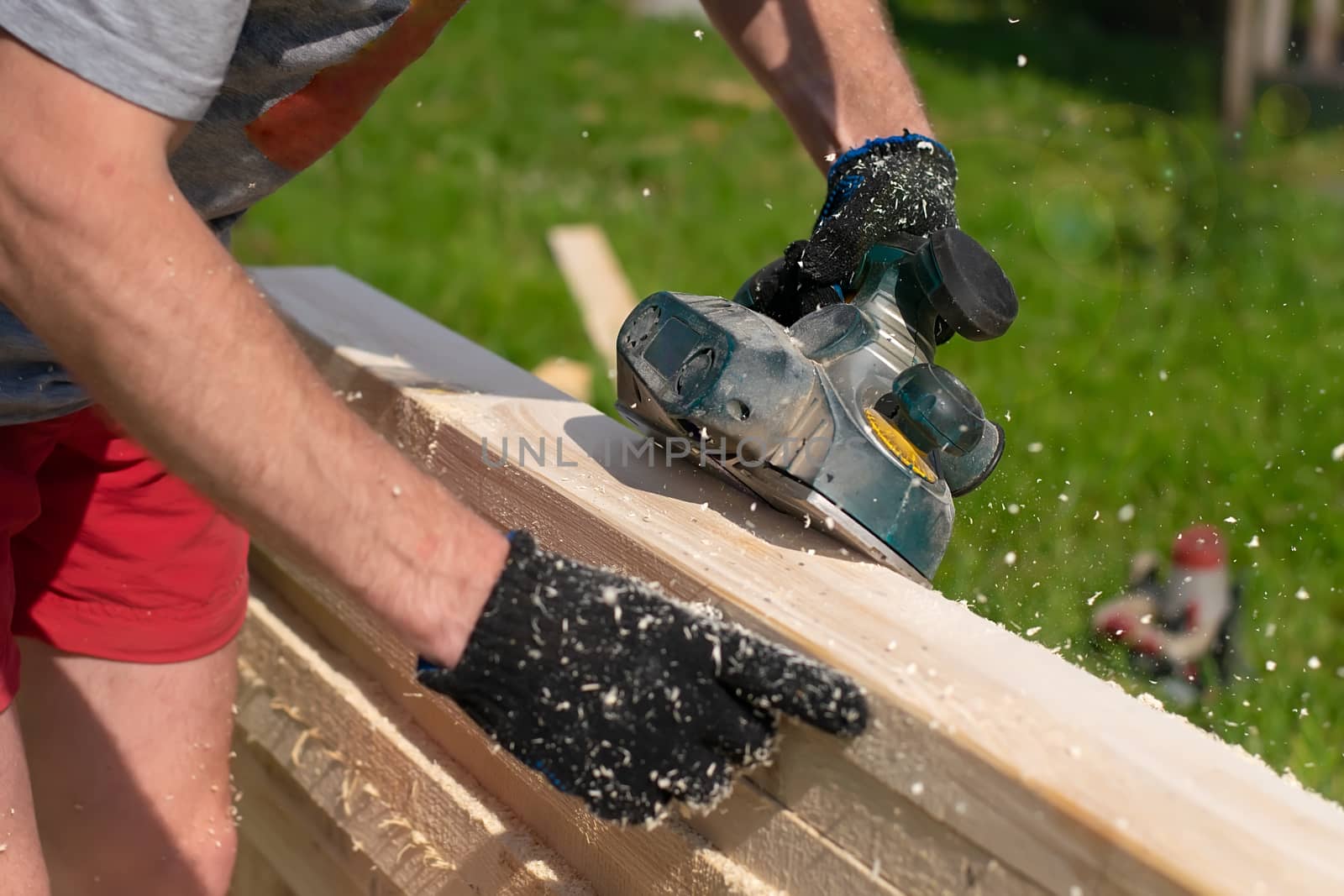 carpenter hands use an electric tool to process raw lumber