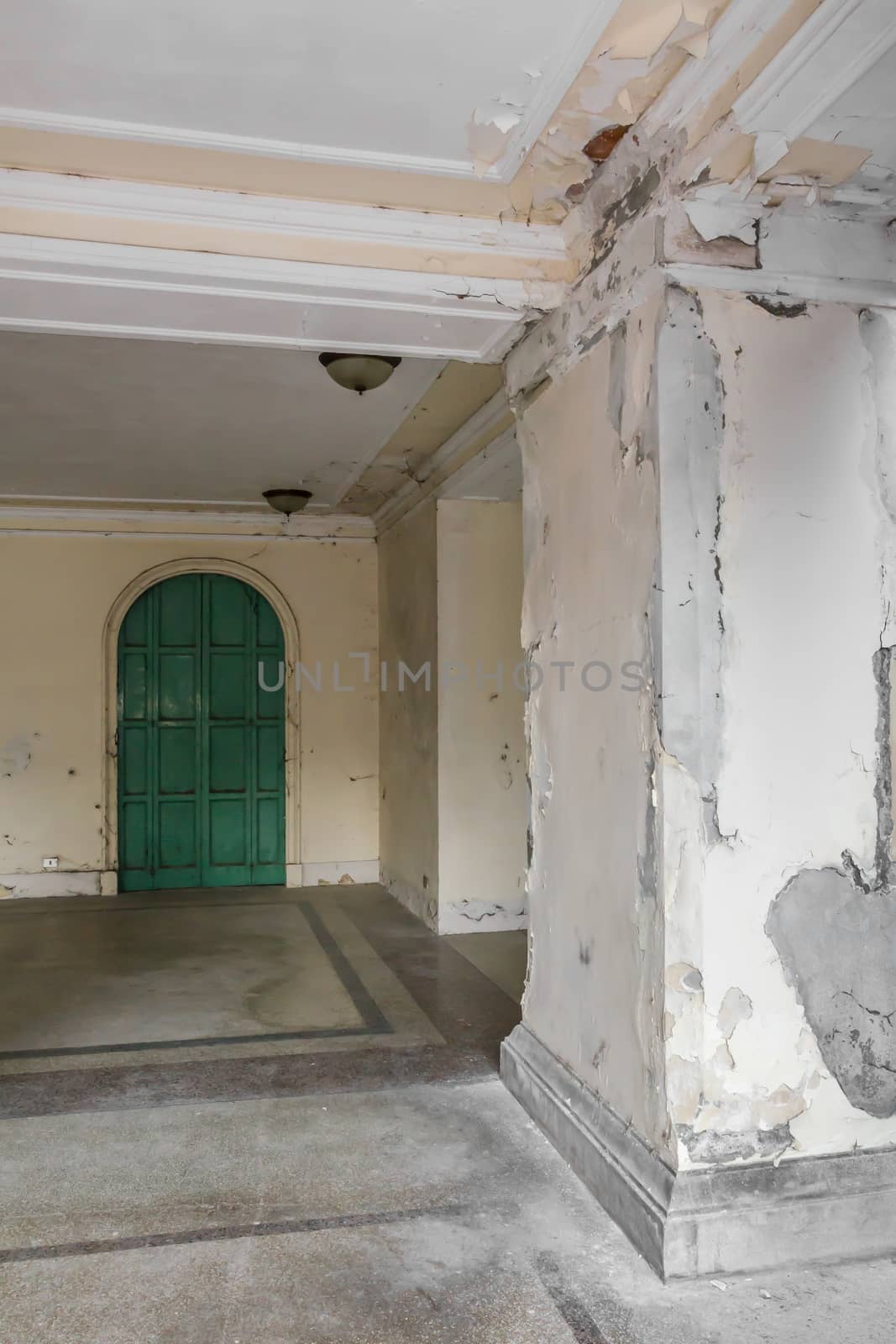 Exterior of an old abandoned hotel with a peeling wall and mold. Ancient green door with old chandeliers on the ceiling.