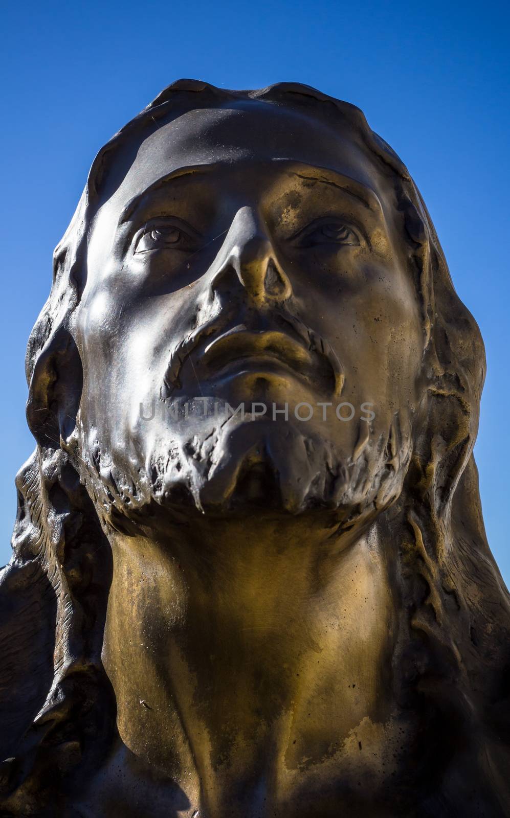 Bronze statue of christ in a blue sky background. Jesus looks up to heaven.