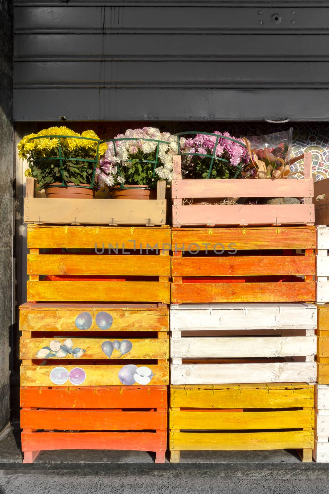 Colored wooden crates with flowers on top, from a florist. The rolling shutter is semi-closed.